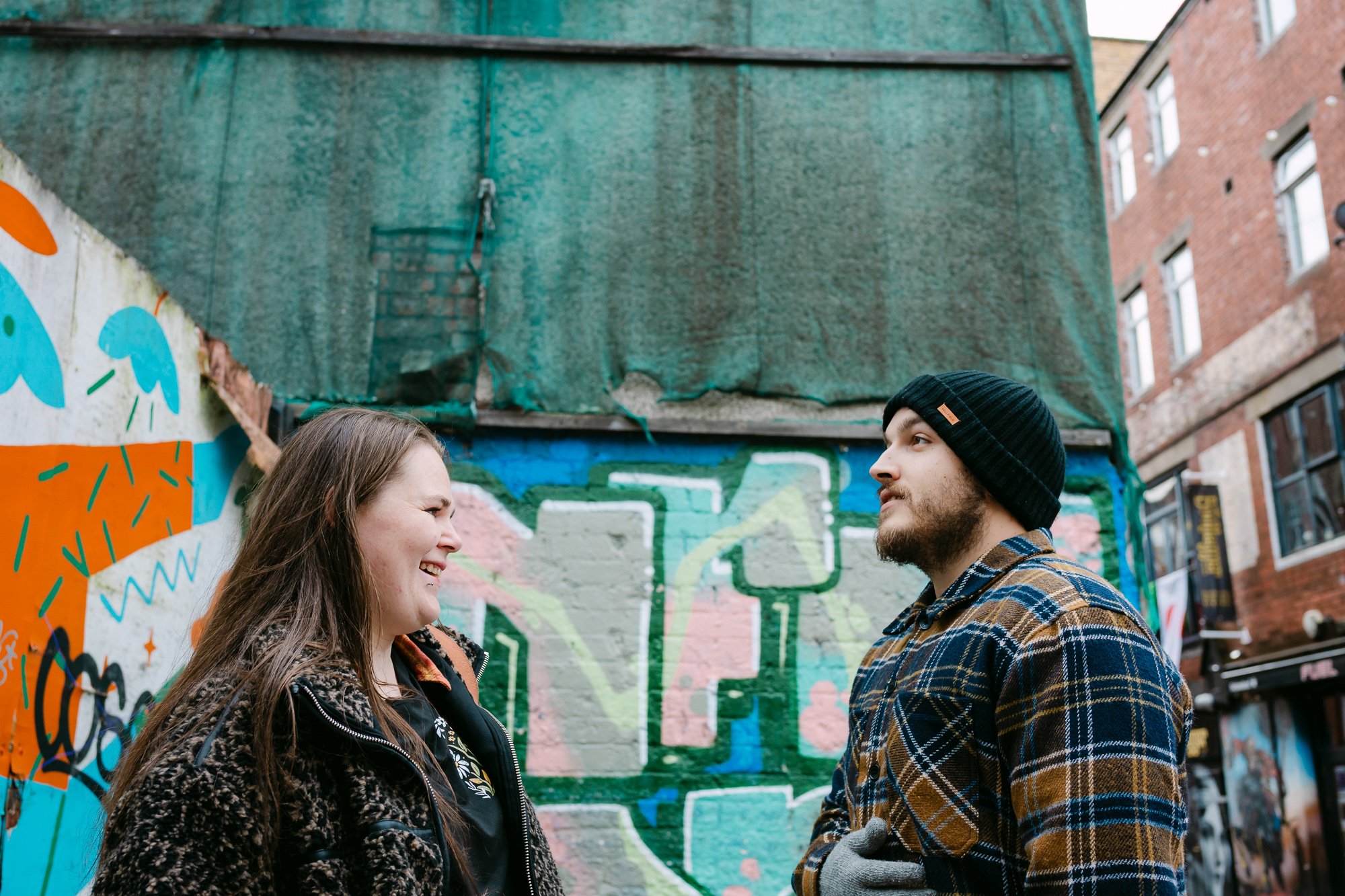 Couple laughing and smiling against a punchy turquoise and orange graffiti mural, fun city engagement photo