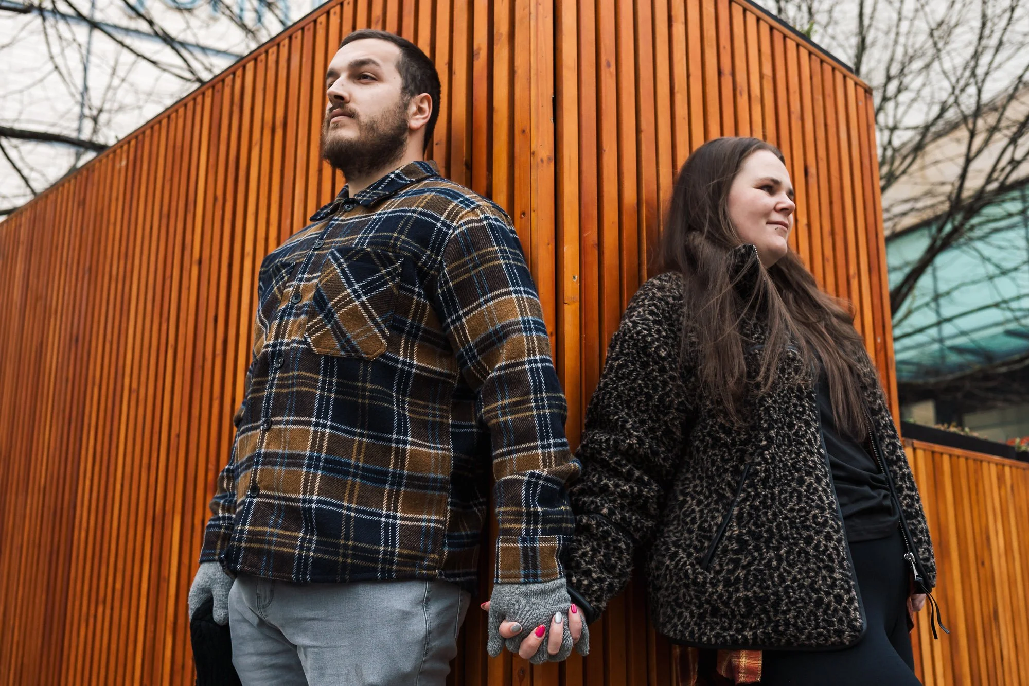 Couple holding hands while leaning on opposite sides of wooden wall corner, creative city engagement photo