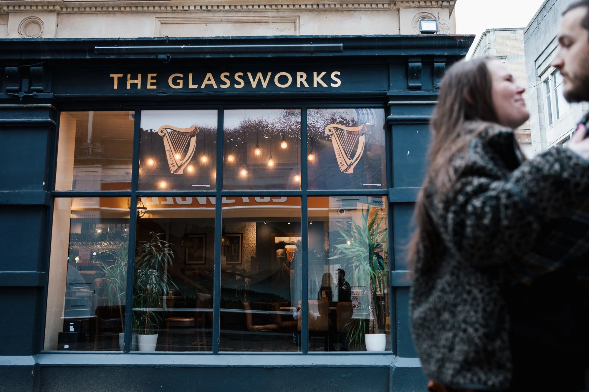 A couple embracing in front of a large window creating their refection on an engagement shoot in Cardiff 