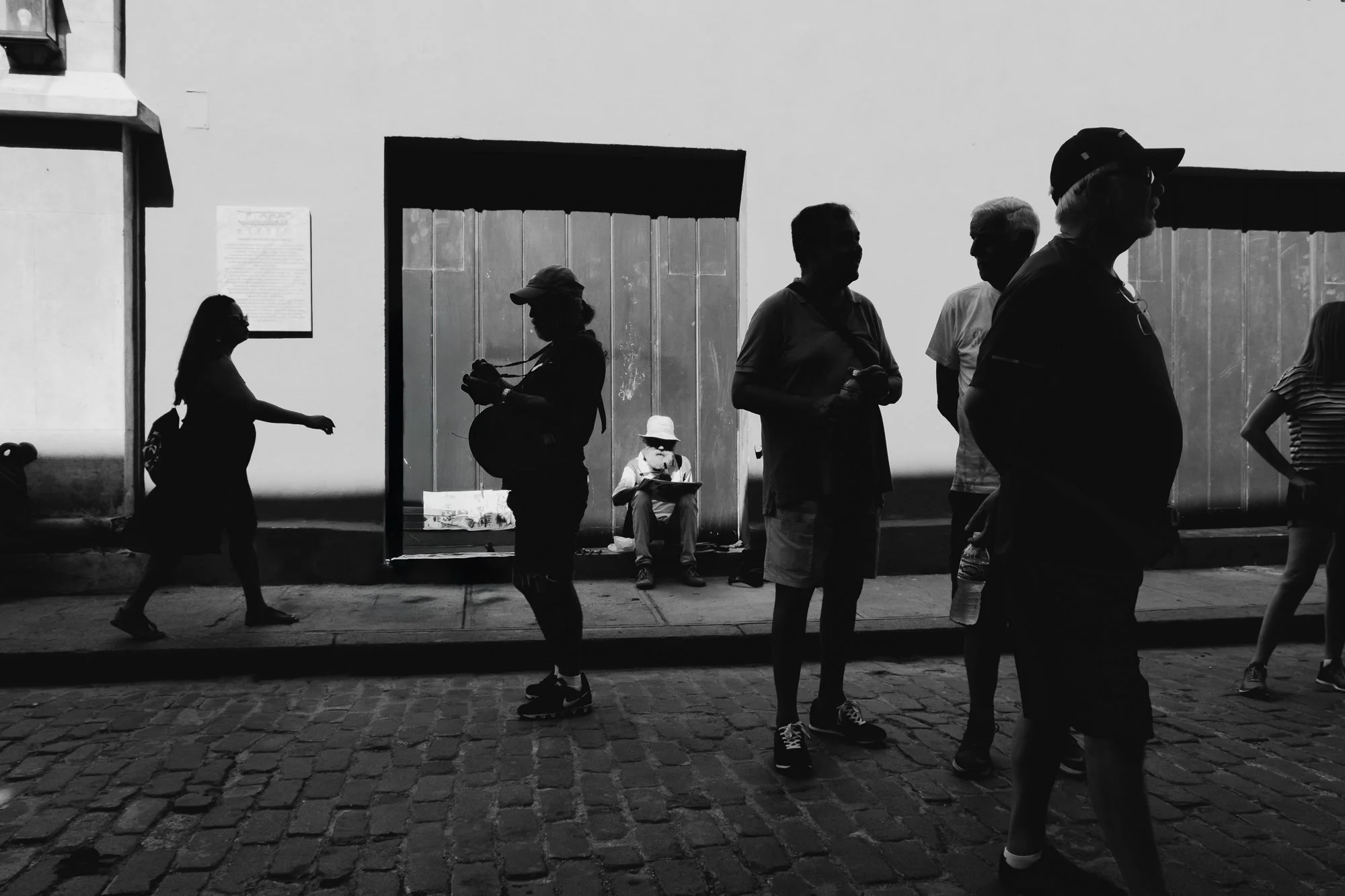 A street artist in Havana painting in the background, illuminated by light and surrounded by the silhouettes of various people. 