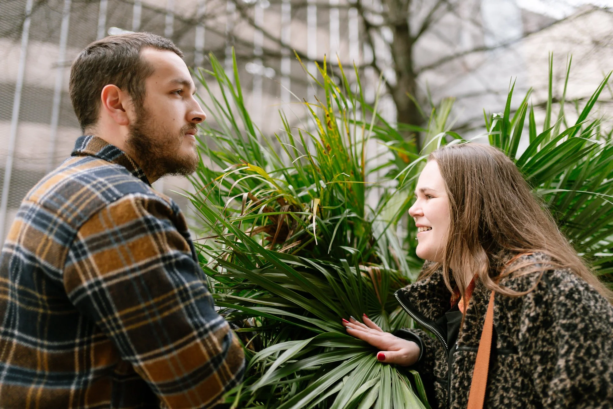 Engaged couple peering over a palm, looking and smiling at each other, creative portrait photography Cardiff