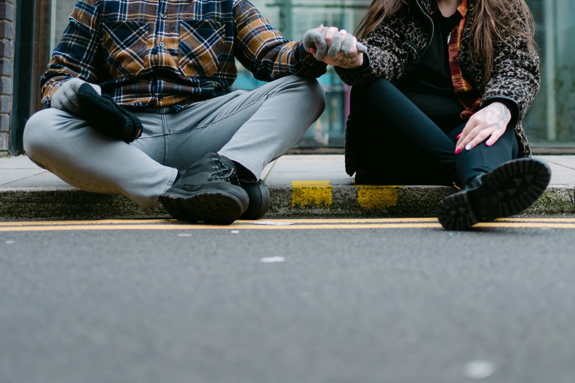 Couple holding hands sitting on a curb being photographed for their engagement 