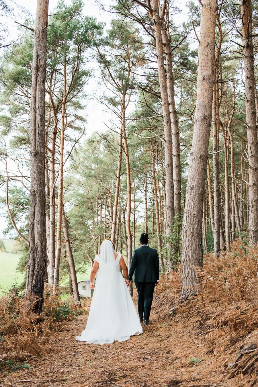 Bride and groom walking whilst holding hands, positioned between trees at the Bridal Barn in Bridgnorth. 