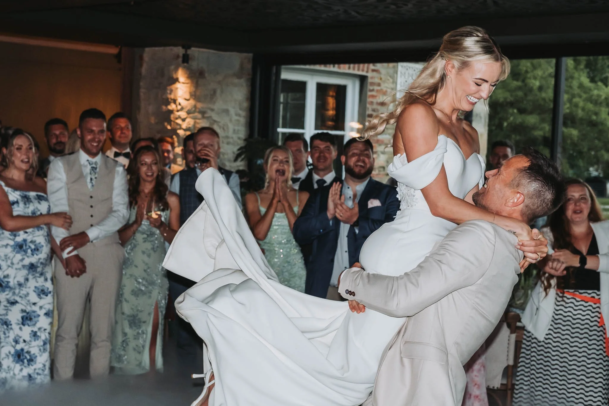A wedding celebration where a bride is being lifted by a groom, with guests in formal attire clapping and smiling in the background at Whitworth Hall.