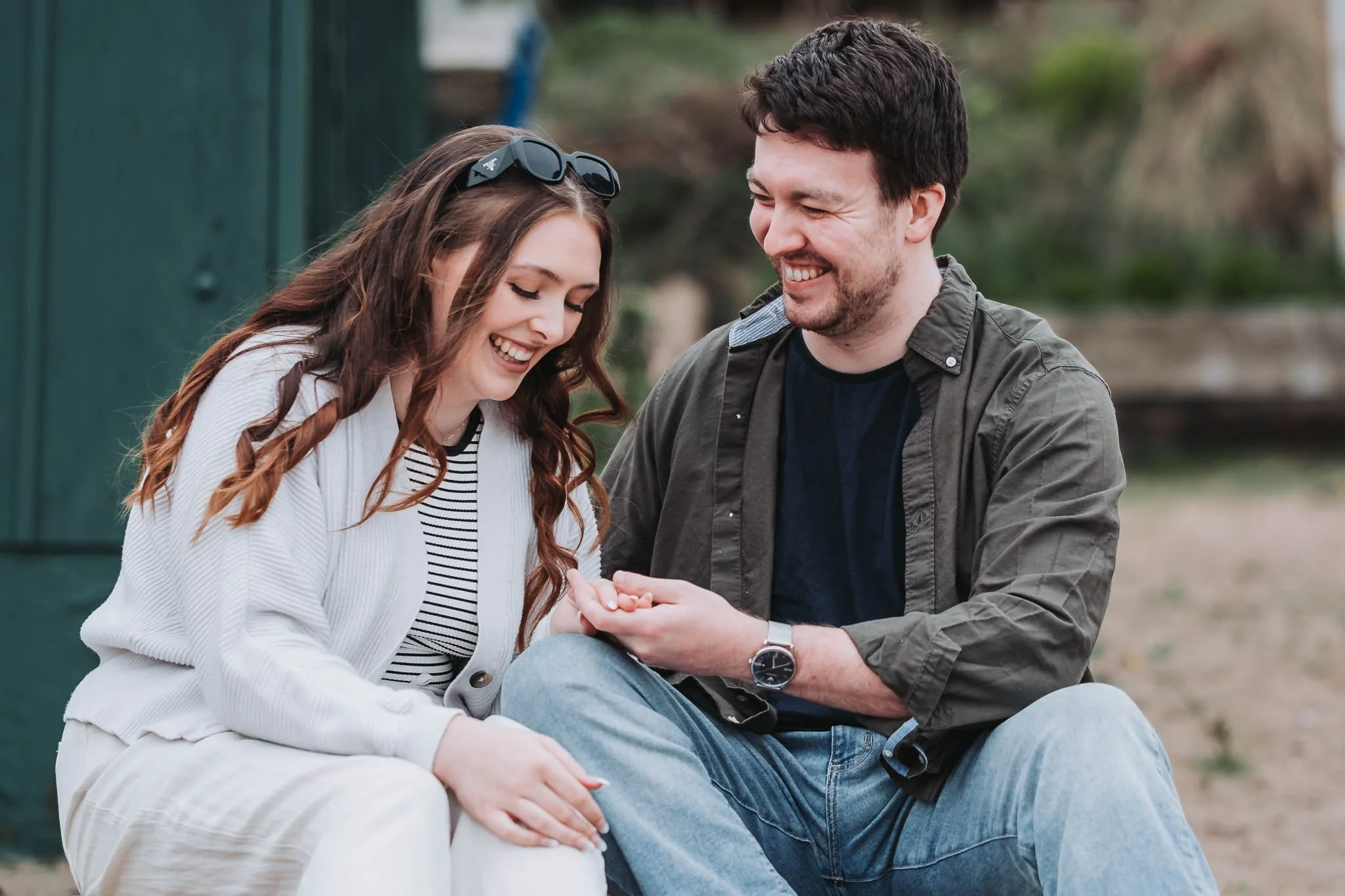 A man and woman sitting outdoors, smiling and looking at each other, sharing a joyful moment.