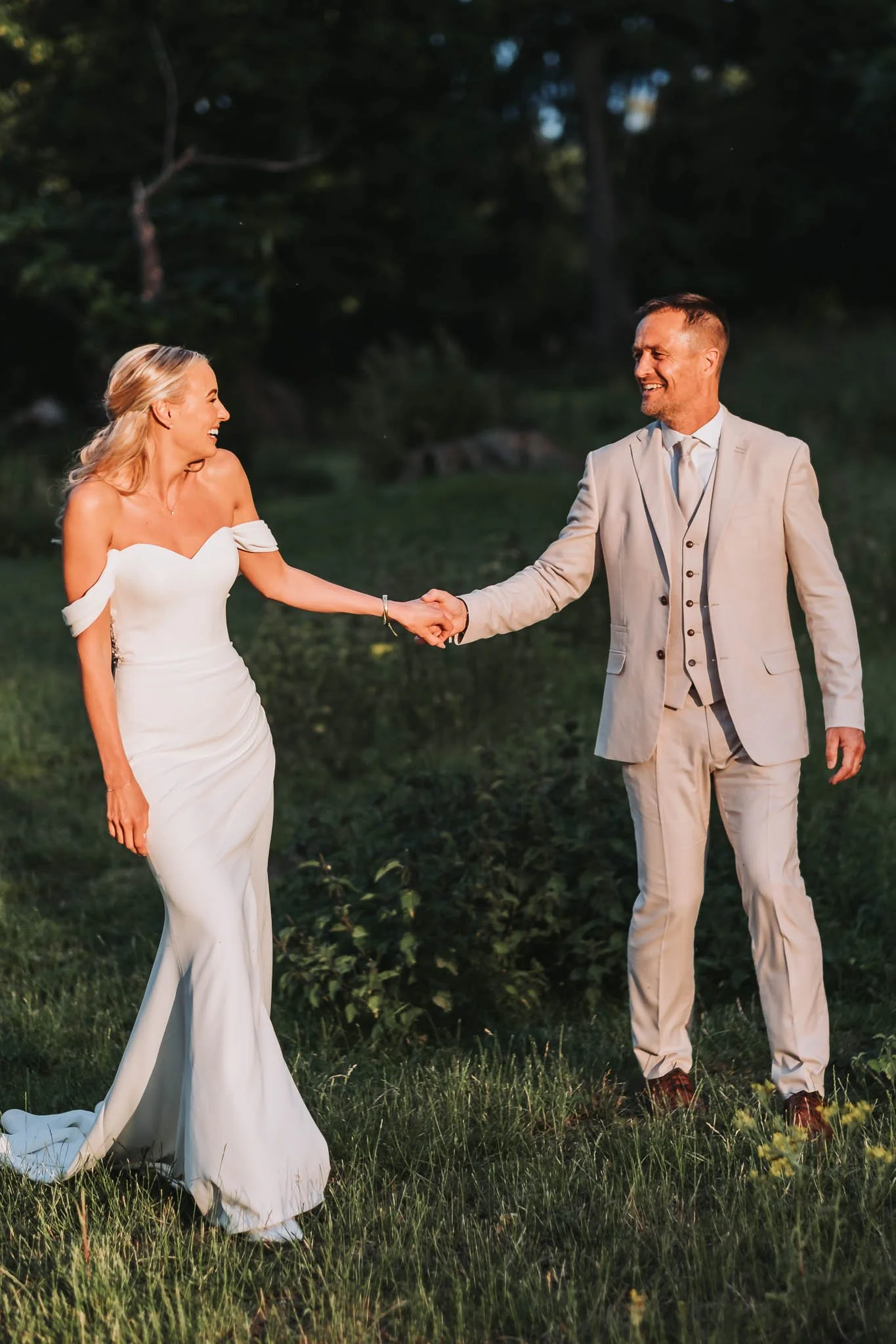 A bride and groom holding hands and smiling outdoors during their wedding ceremony at sunset at Whitworth Hall.