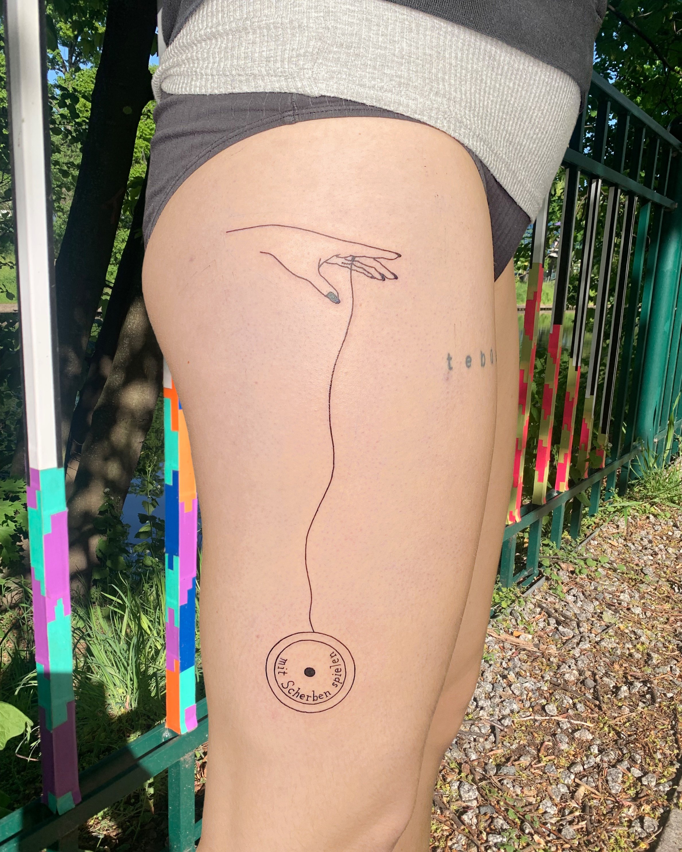 simple tattoo of a hand holding a mit scherben spielen yoyo made with black ink on upper leg.JPG