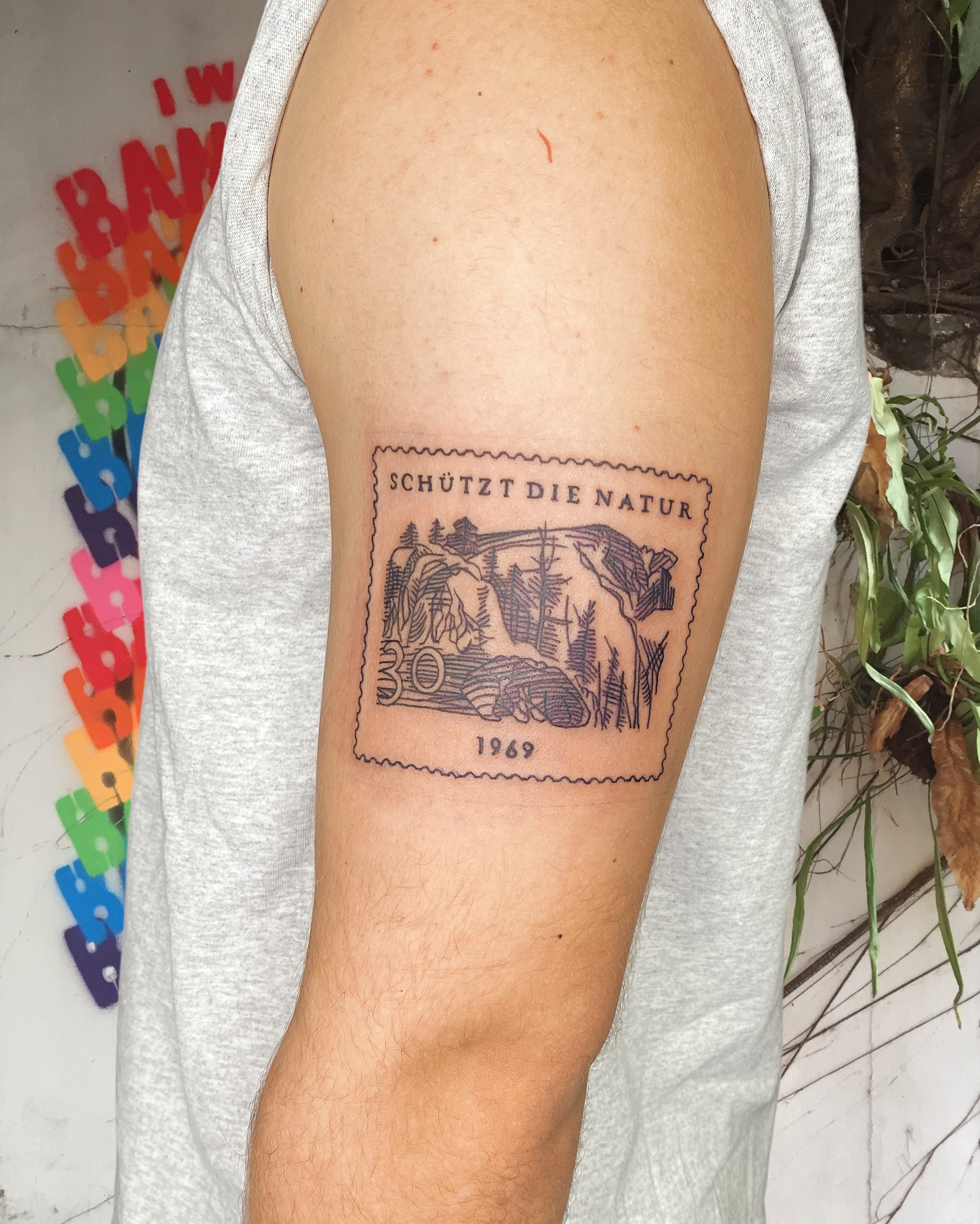tattoo of a stamp schutzt die nature 1969 black ink on upper arm.JPG