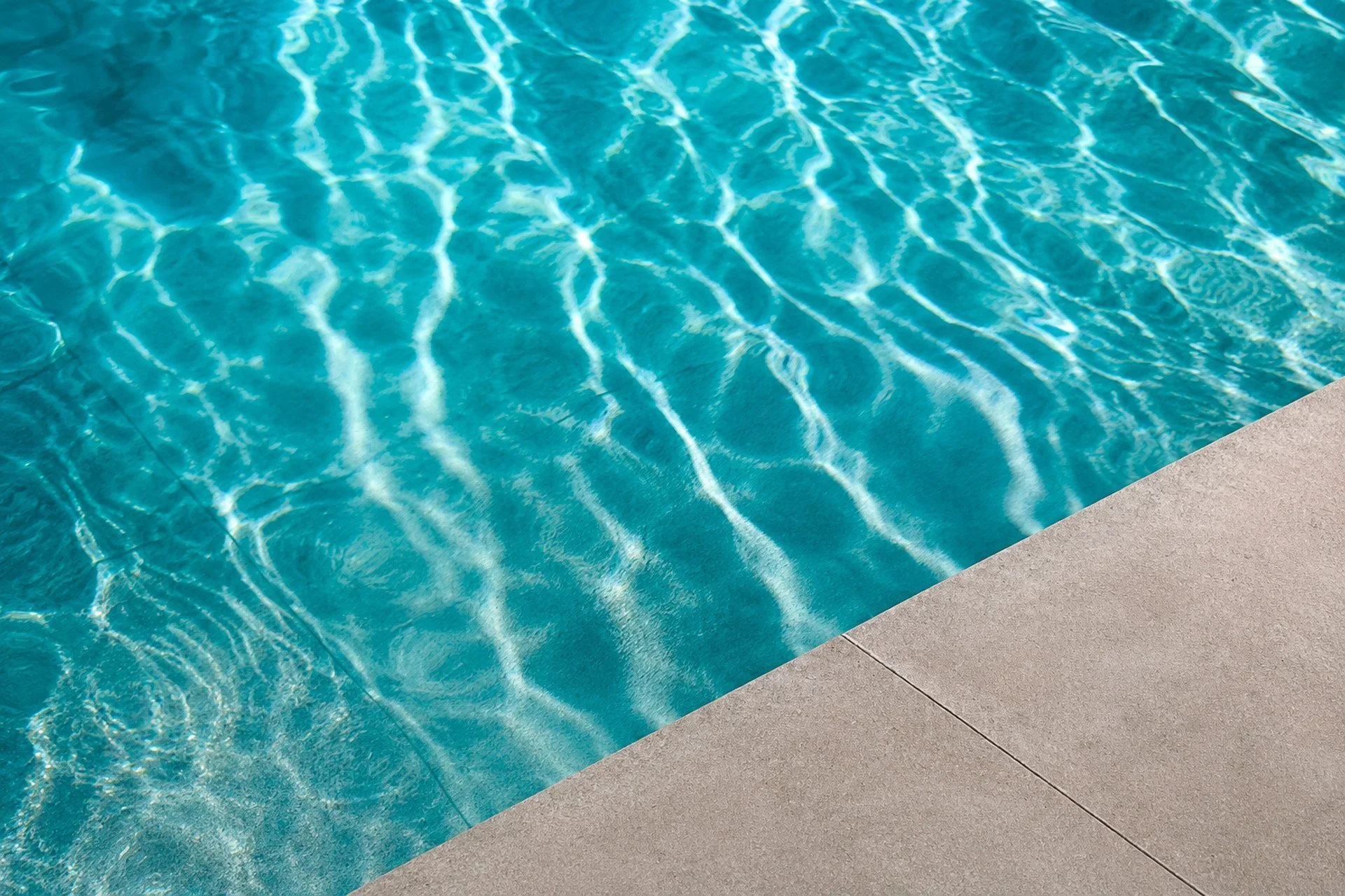 Close-up of a swimming pool with clear blue water and gentle ripples, next to a concrete pool deck.