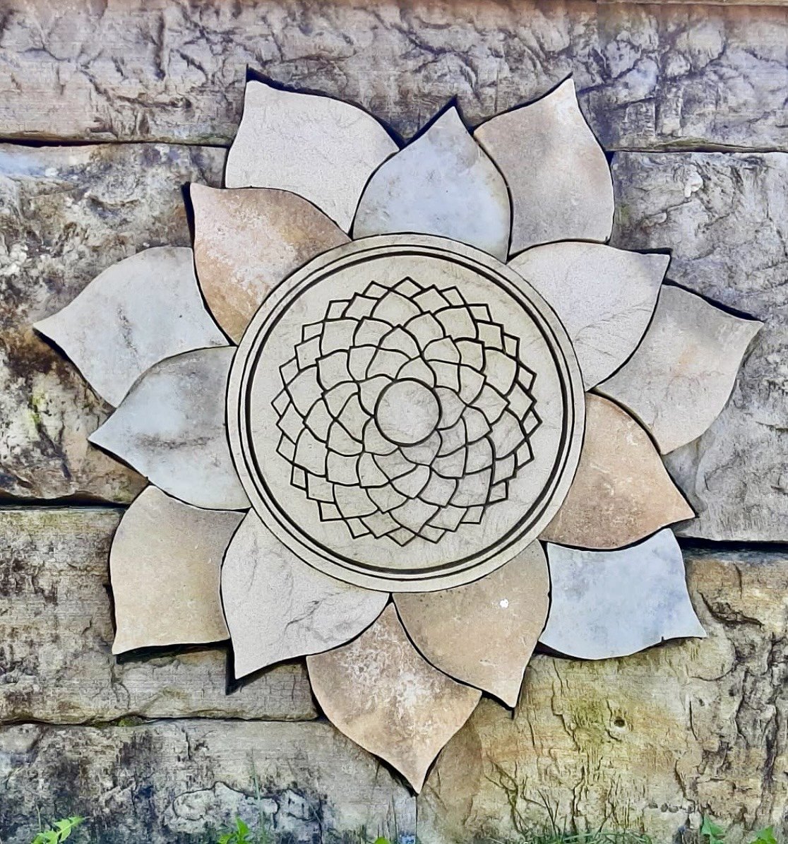 Decorative wall art featuring a carved lotus flower design with layered petals, mounted on a stone wall.