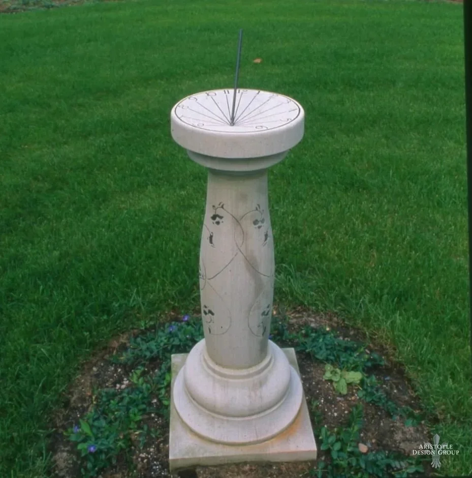 A sundial placed on a stone pedestal on a patch of land surrounded by grass.
