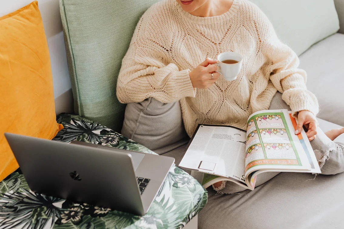 kaboompics_The woman is drinking tea on the couch, reading the newspaper and using a laptop.jpg