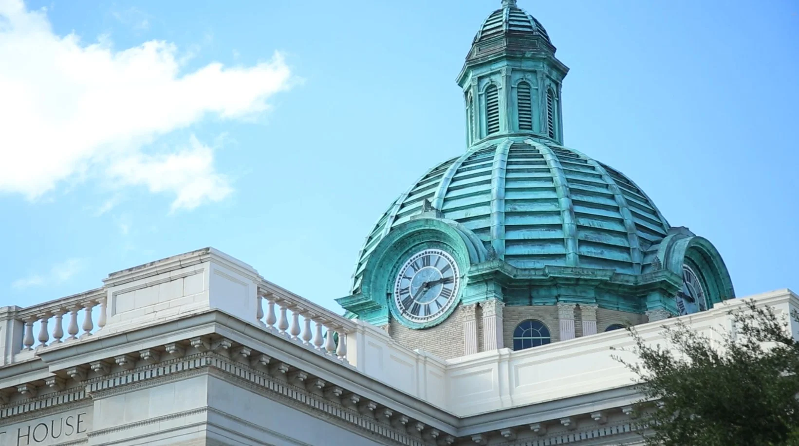 A green, domed clock tower above a courthouse.