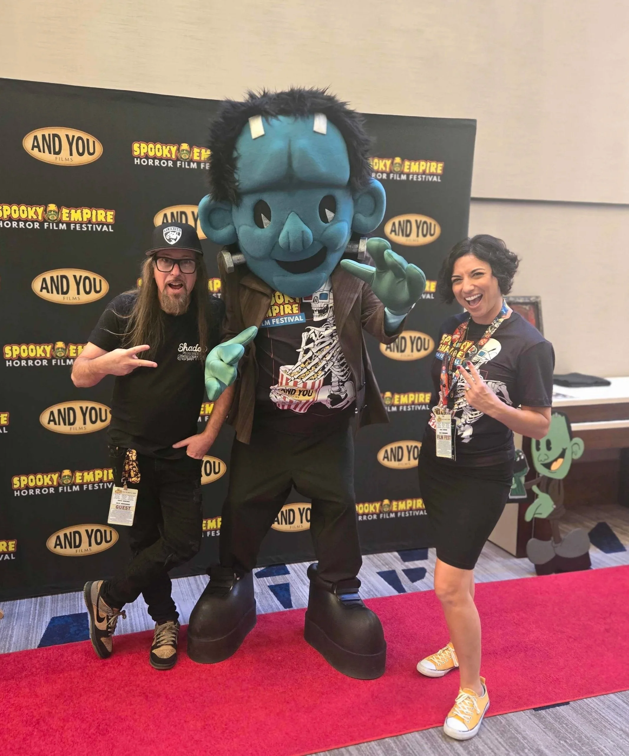 A man and woman pose with a mascot resembling Frankenstein's Monster.