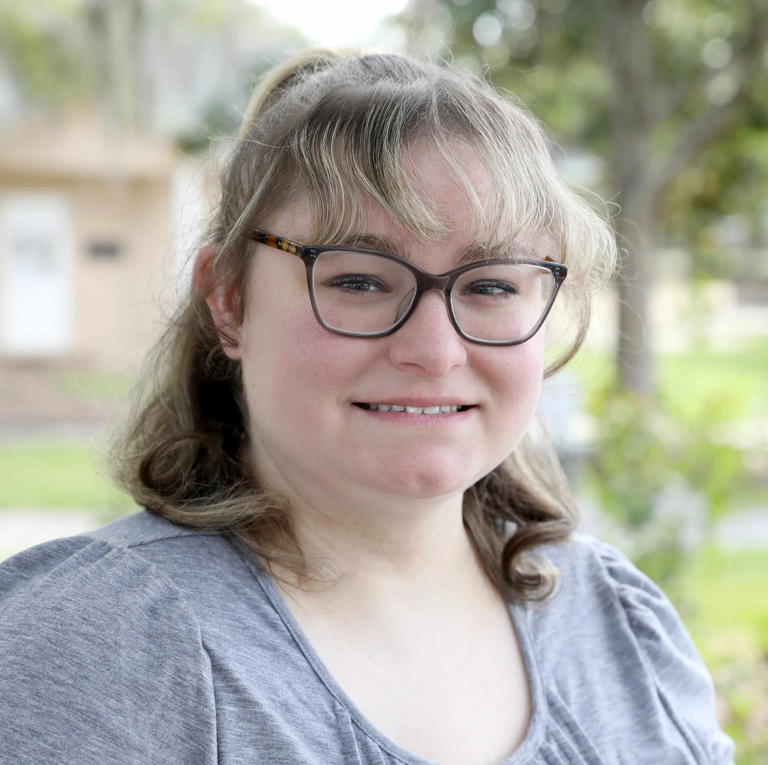 The smiling face of a woman with glasses and blonde hair.