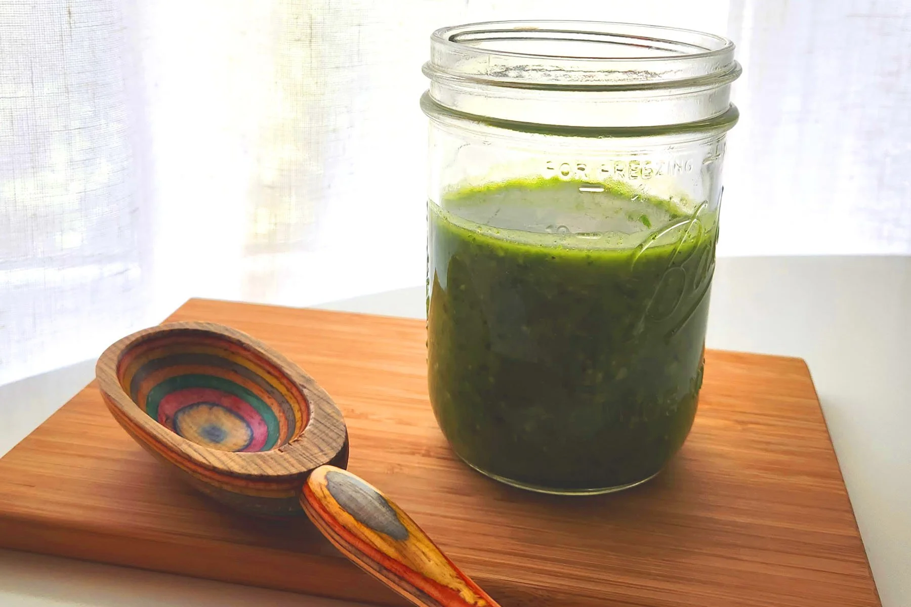 A mason jar filled with a bright green blend of fresh basil, parsley, rosemary and garlic with oil to add flavor to foods before grilling, roasting, air frying, seaing, and steaming.