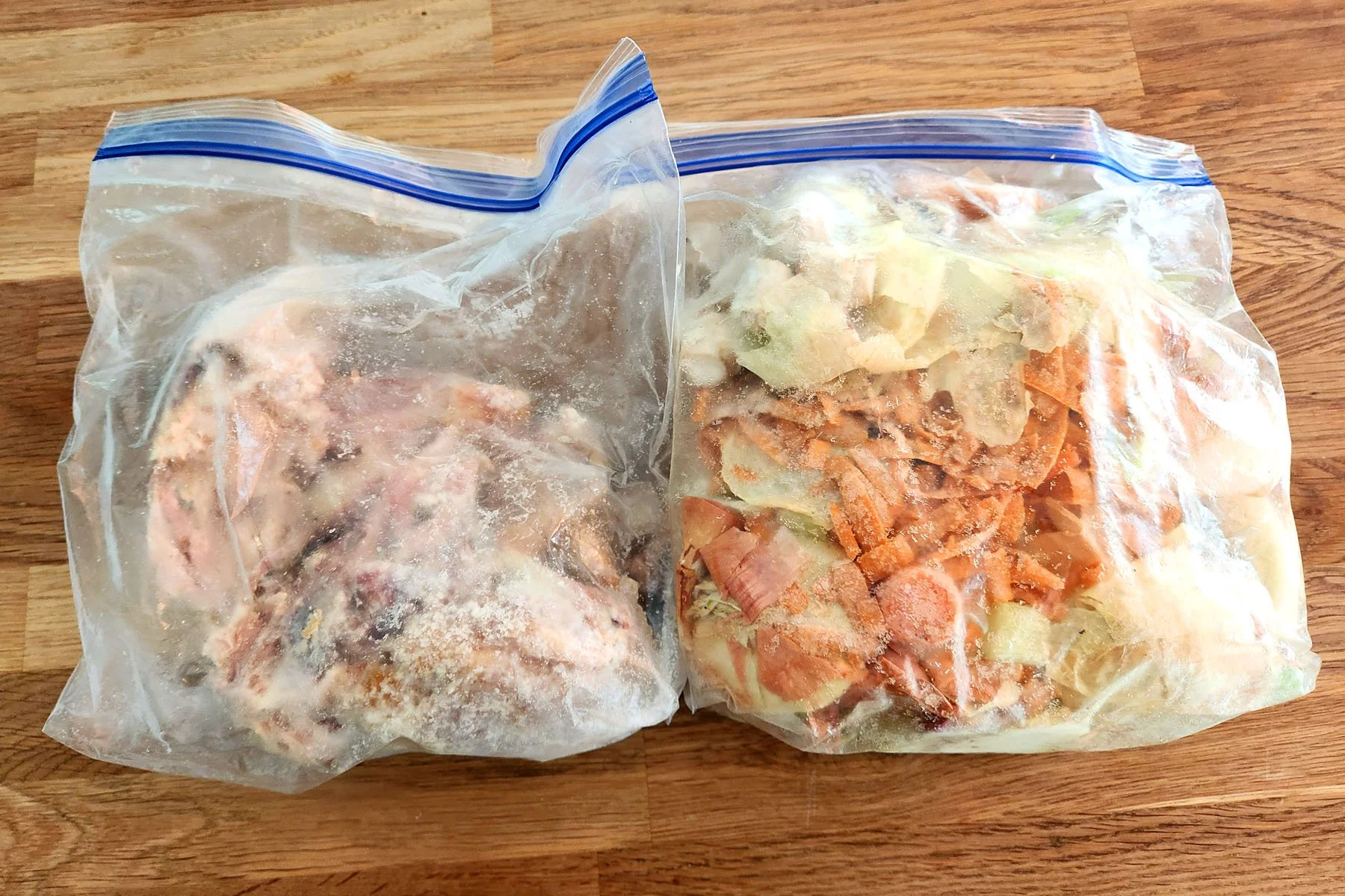 A bag of rotisserie chicken bones and a bag of vegetable scraps from the freezer to be used to make rich chicken stock out of food waste.