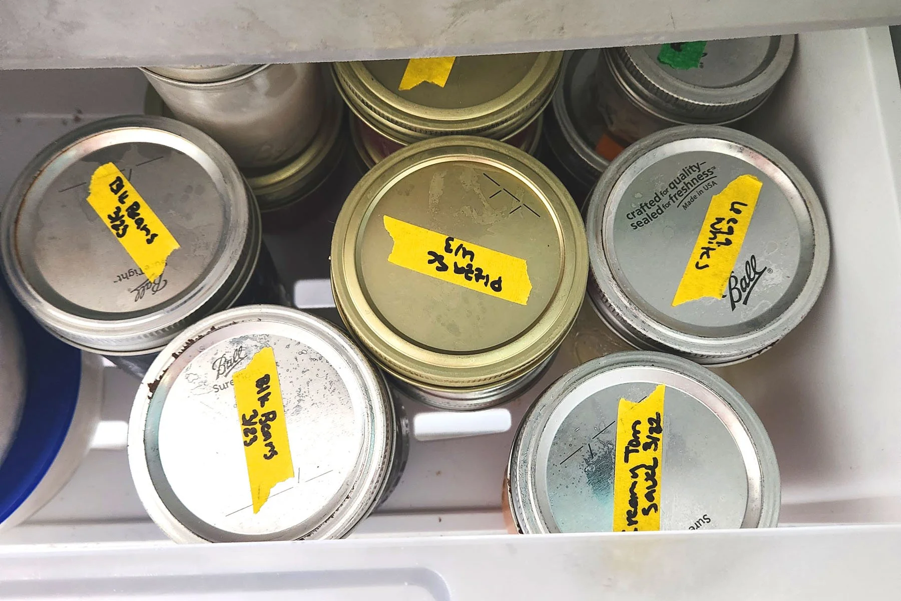 Freezer drawer filled with wide-mouth mason jars filled with cooked black beans, pizza sauce and more for easy weeknight meal prep.