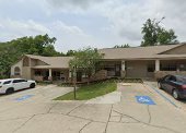 Single-story building with a parking lot, located in a suburban area with trees and a flag in front.
