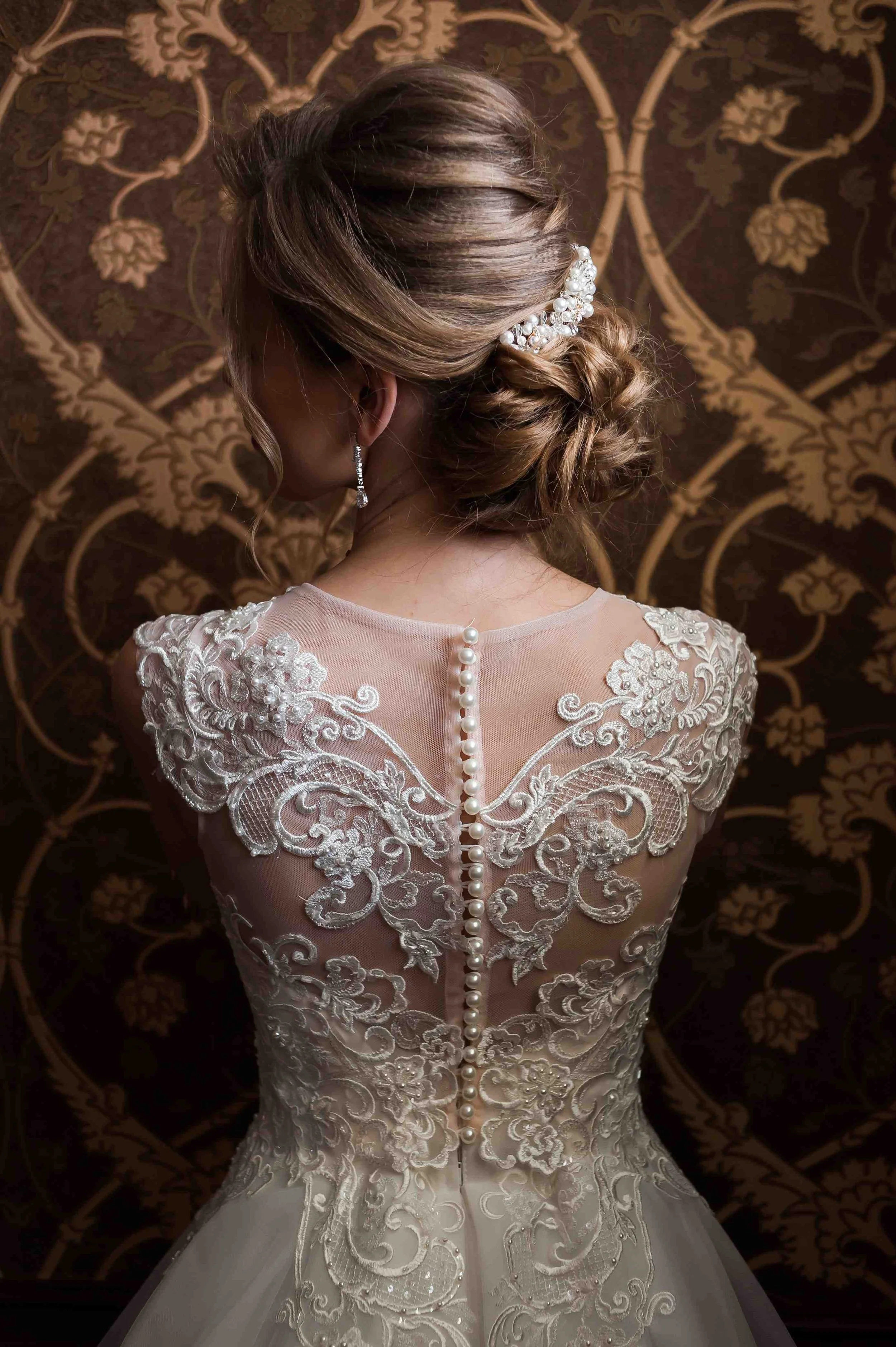 A woman in a bridal gown posing with her back to the camera, showing a line of pearls along the zipper of the dress