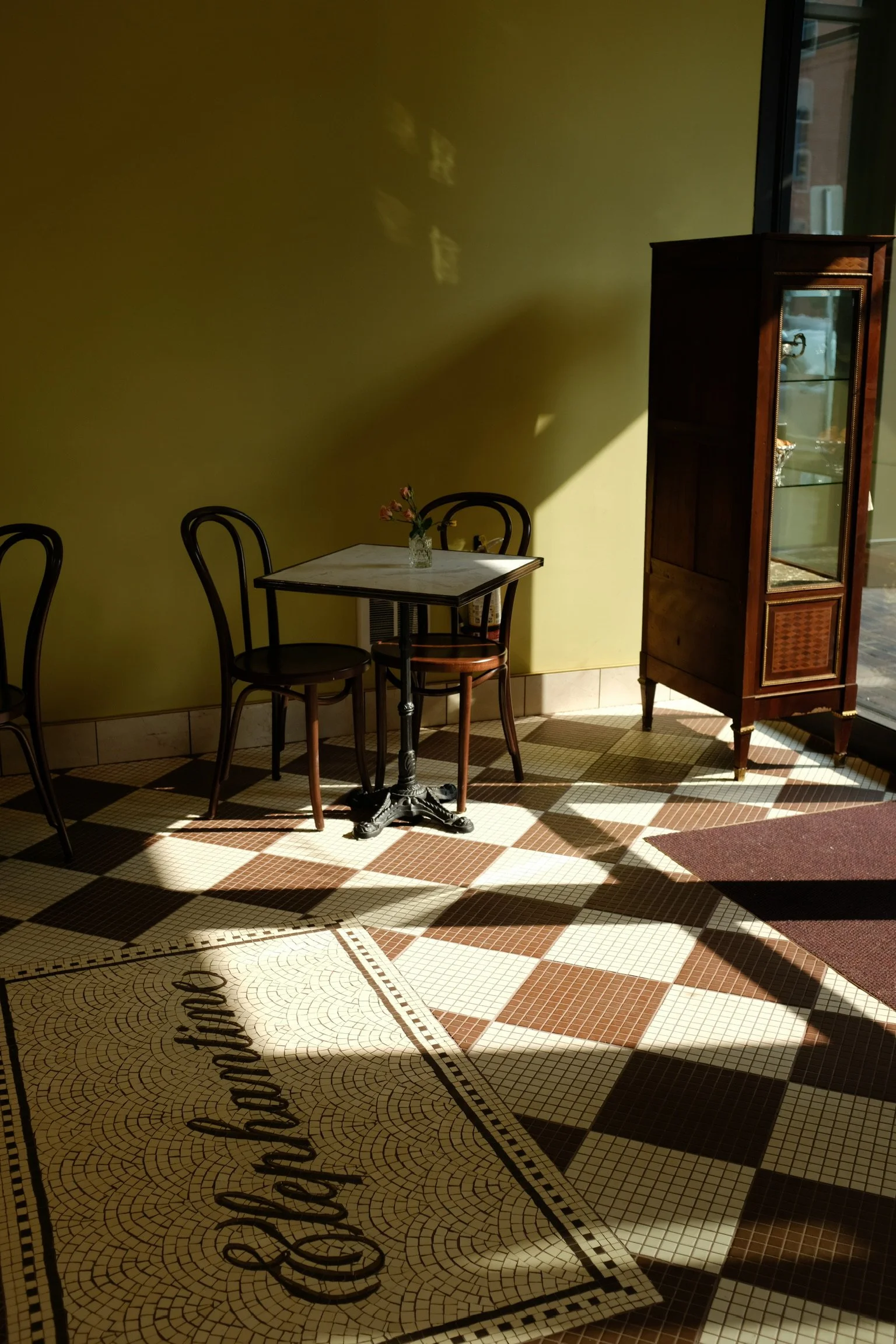 Interior of Elephantine Bakery’s café in Boston’s Fort Point, featuring a classic bistro table and chairs in the afternoon sun