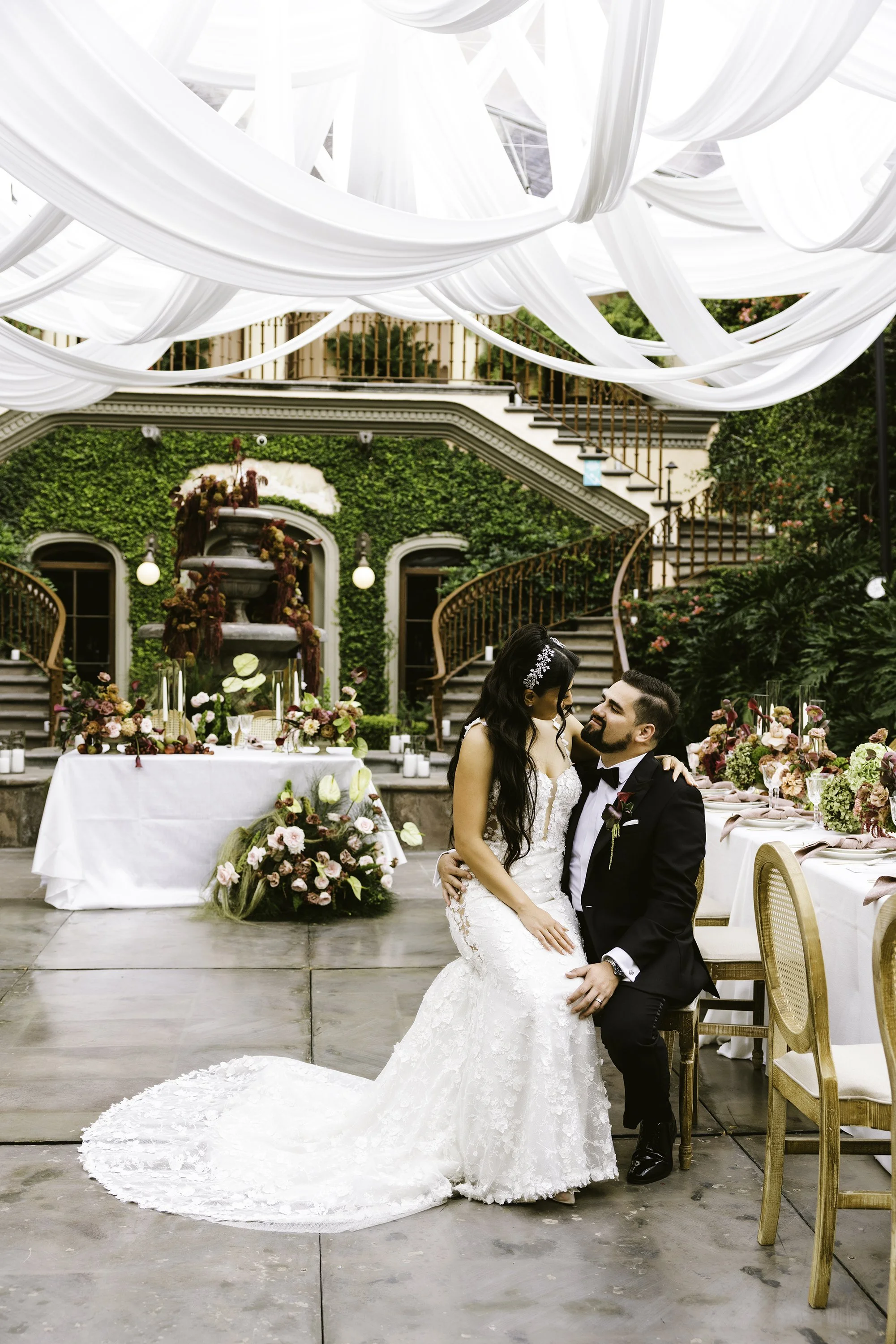 A bride and groom sharing a moment at their wedding reception indoors, decorated with flowers and greenery.