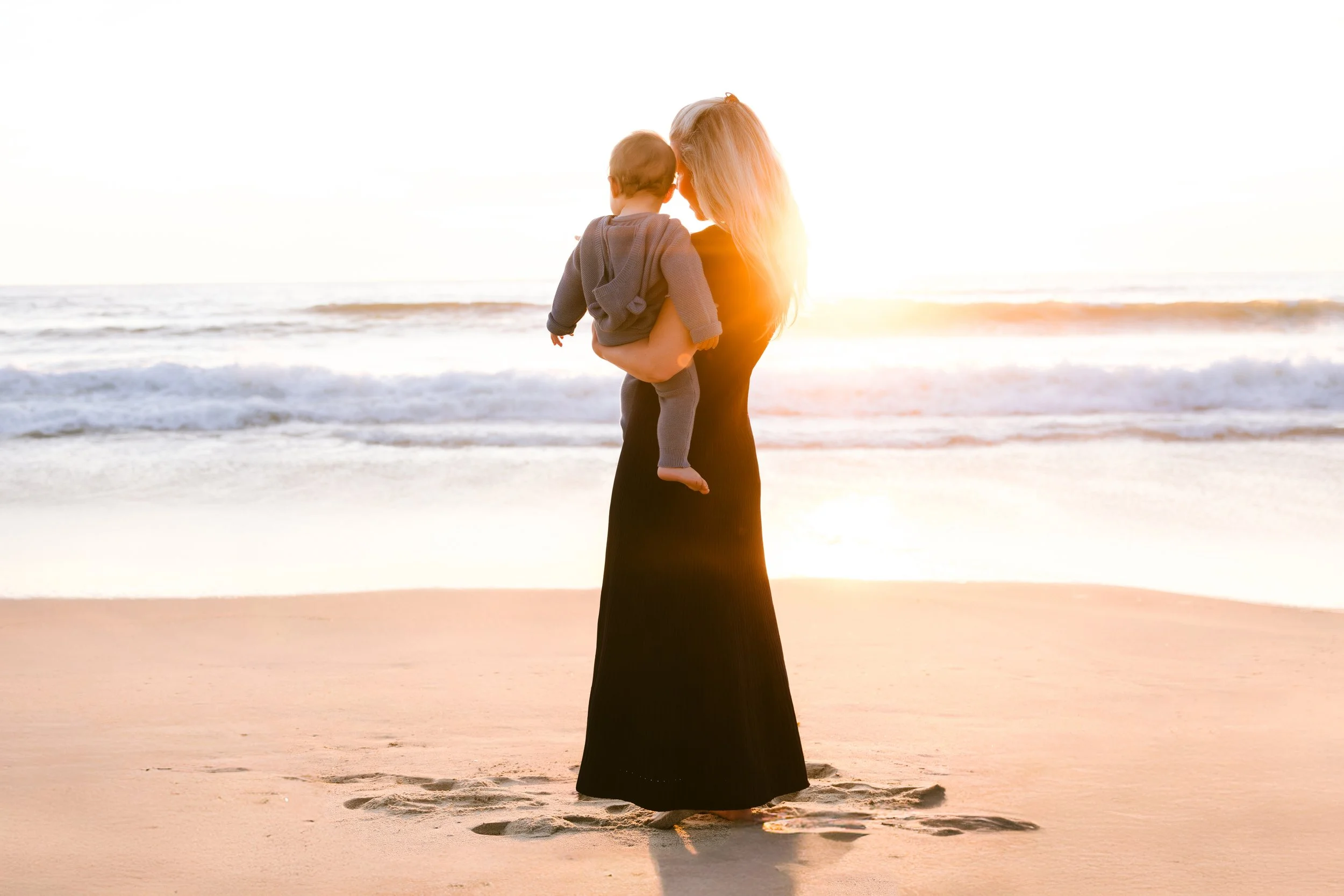 Woman holding a child on a beach during sunset.