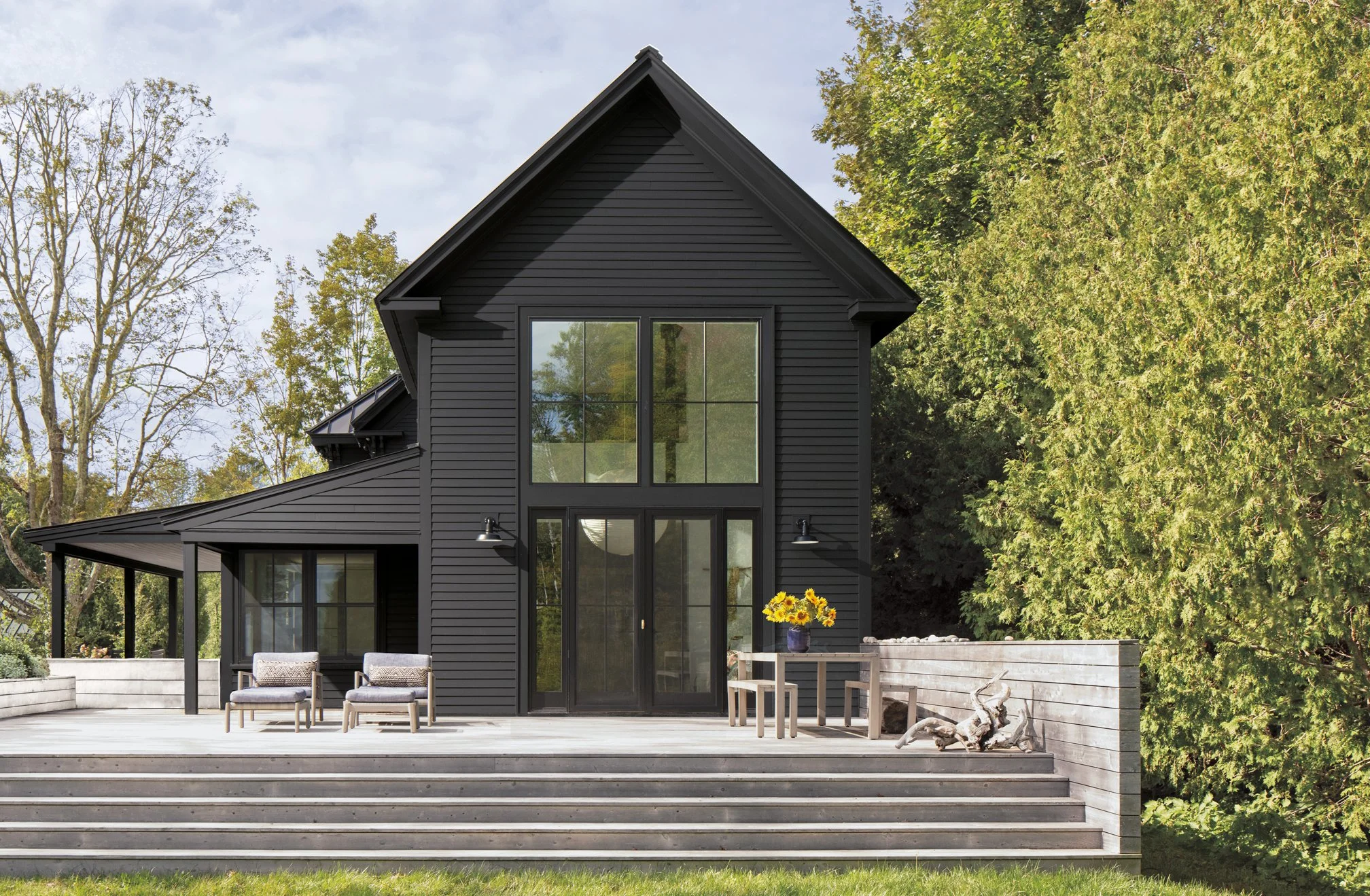 Mountain modern black exterior home with large windows and a stained wood deck, surrounded by trees and reflecting current exterior design trends.