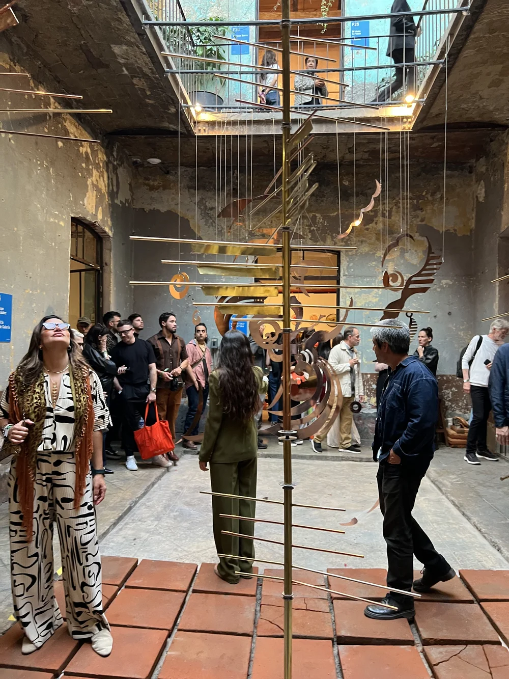 Cristina Lugo with guests beneath a brass mobile sculpture in a Mexico City courtyard during Art Week