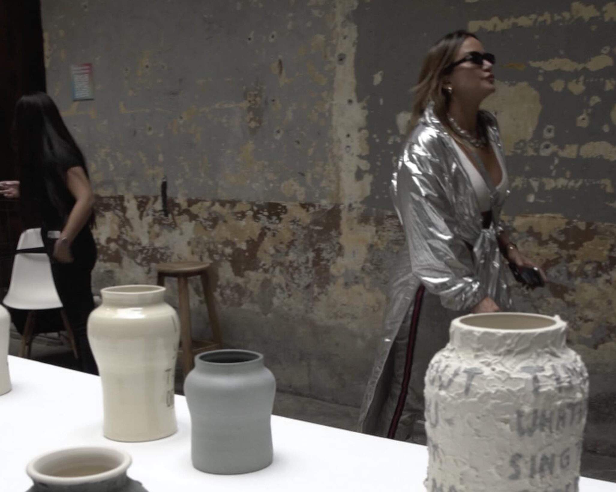 Visitor in a silver coat among ceramic vessels at a Mexico City gallery during Art Week