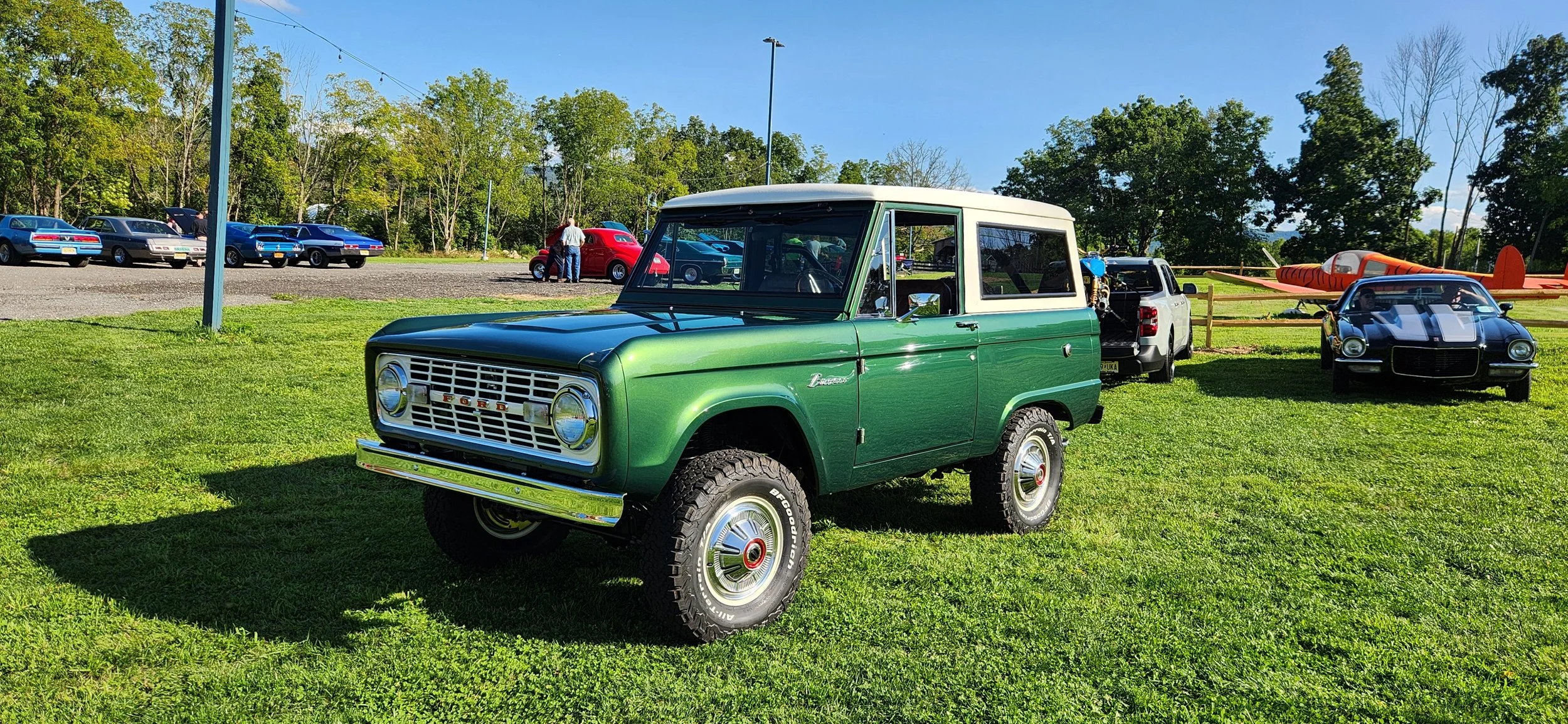 Refurbished vintage Ford Bronco with green exterior and white hardtop, displayed outdoors on grass.