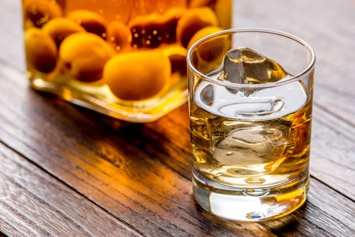 Un bicchiere di whisky con ghiaccio su un tavolo di legno, con una bottiglia di whisky dietro.