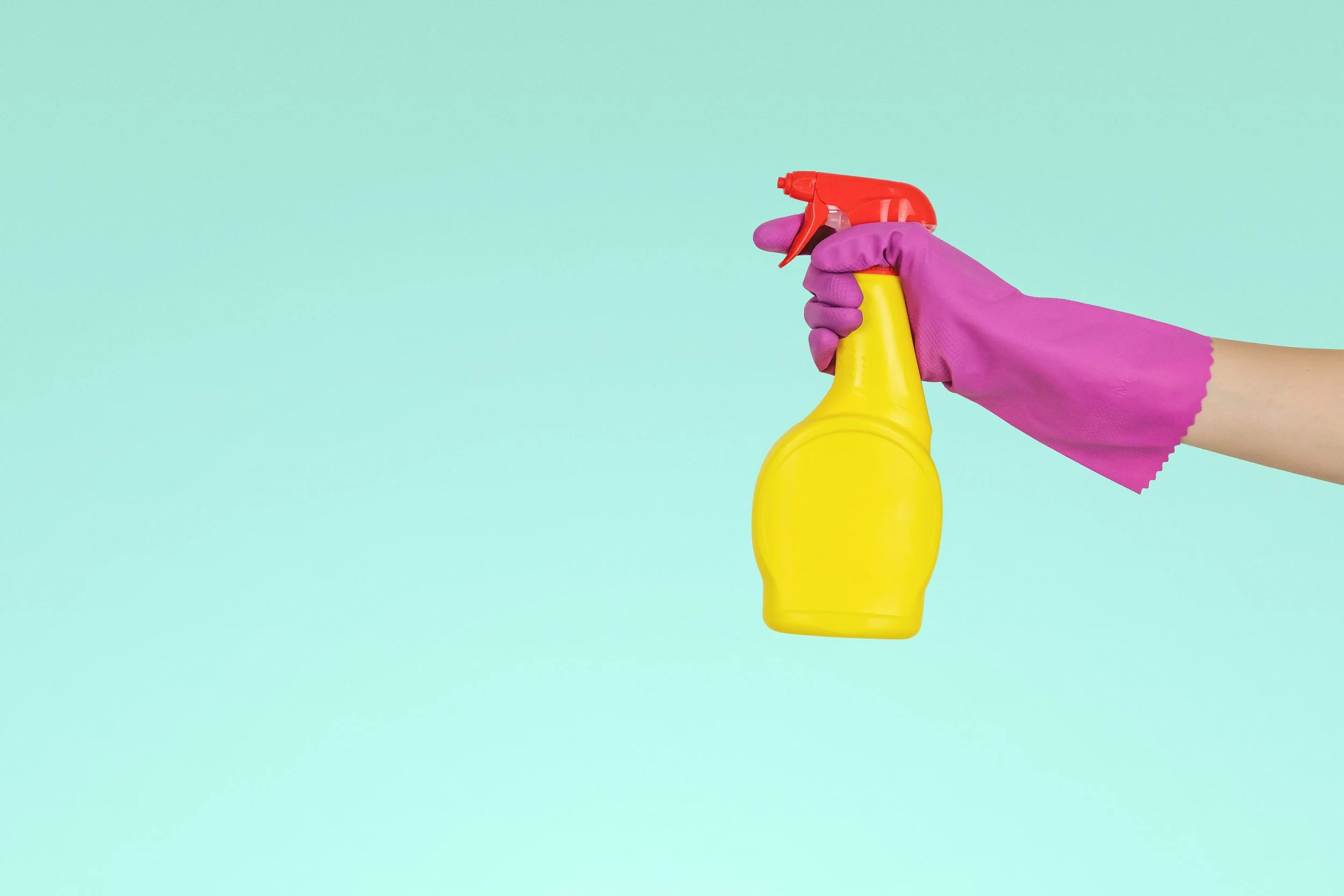 a hand with a pink cleaning glove holding a yellow cleaning spray bottle; fertility los angeles home