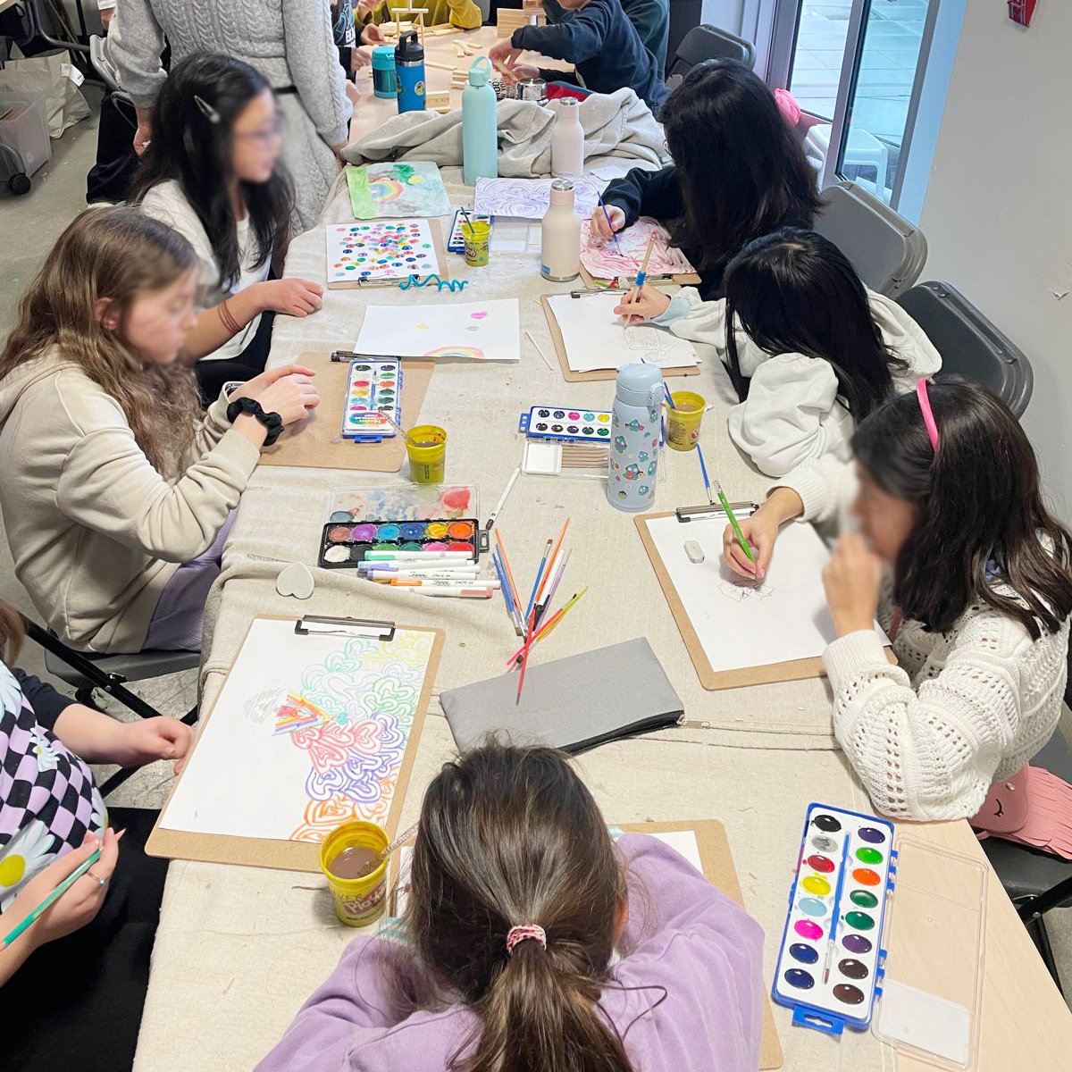 Kids sitting at a table painting and drawing with watercolour paints