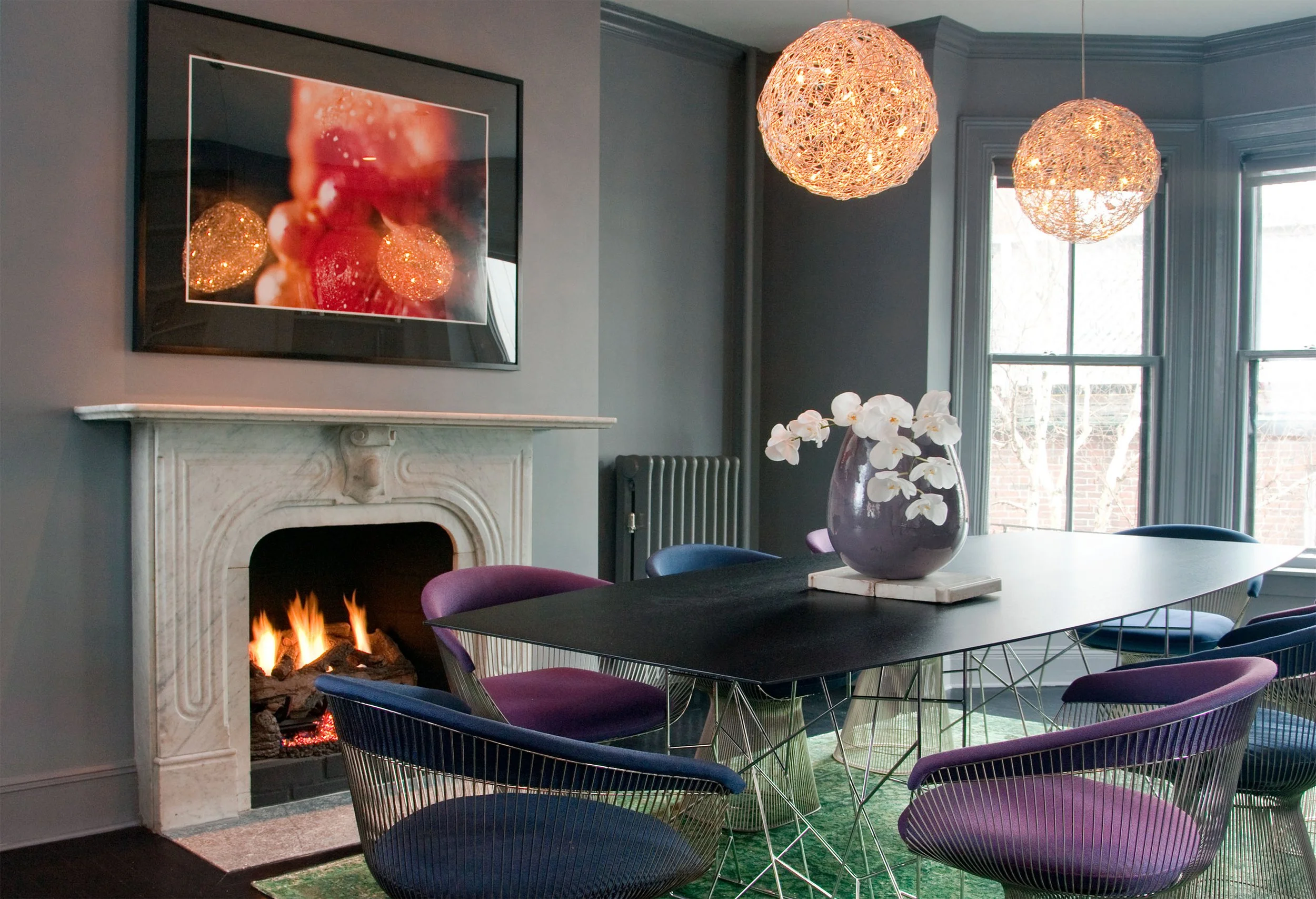 A renovated historic dining room painted in a moody gray color, pairing contemporary furnishings with an ornate marble mantel.