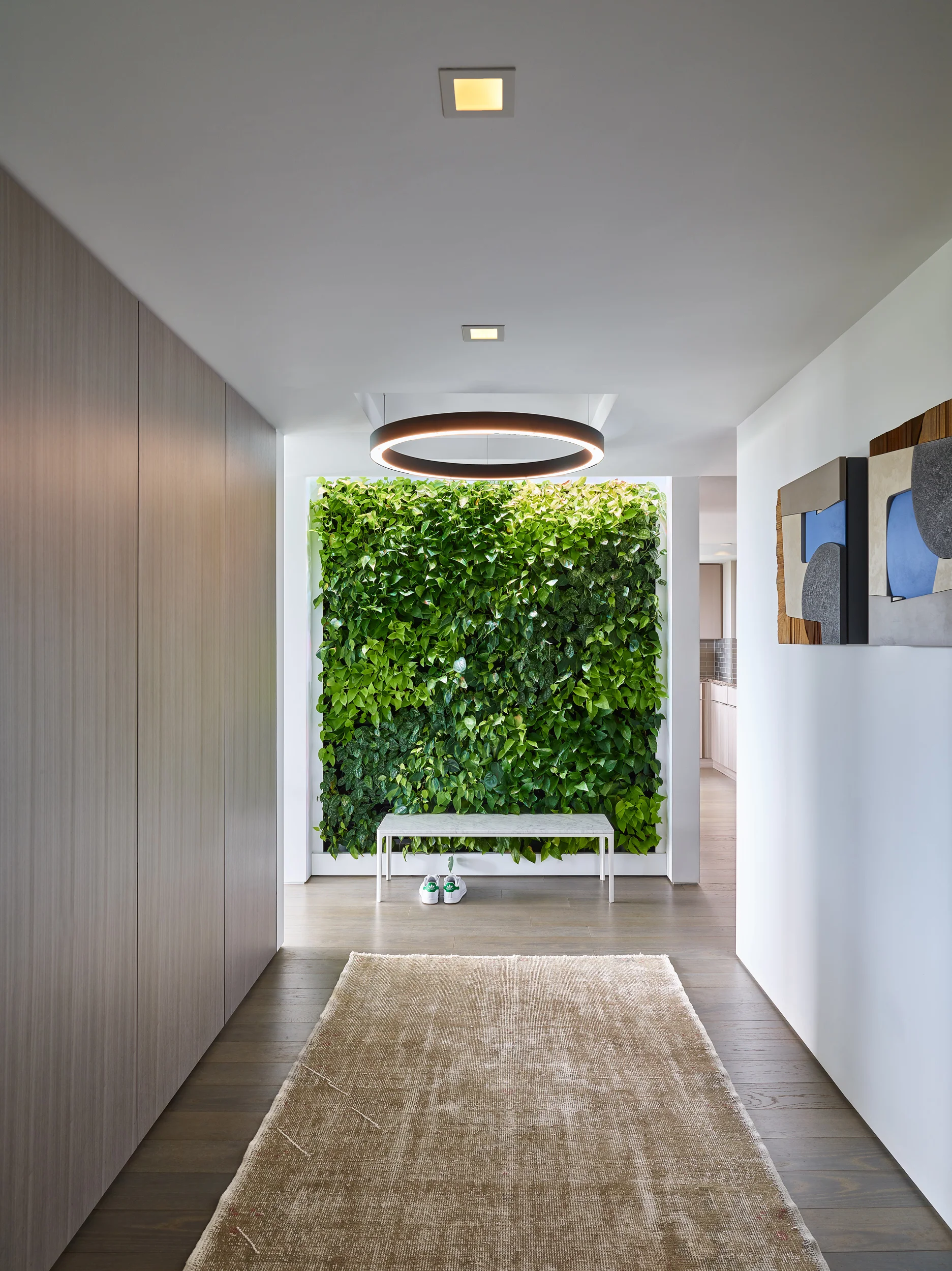 DOWNTOWN LIVING LOCATION Boston, MA COMPLETED 2018 ARCHITECT & INTERIOR DESIGN Walker Architects GENERAL CONTRACTOR The LaGasse Group STONE SUPPLIER & FABRICATOR Cumar PHOTOGRAPHER Jared Kuzia Photography Our clients, downtown academics with grown children, sought to combine two mid-rise apartments to gain an unparalleled elevated view sweeping from the dome of the Boston State House westward to the riverfront campuses of MIT and Harvard. Because the owners were already comfortably at home in one of the apartments, the added second unit was designed as additional spaces for relaxation, with accommodations for billiards and darts, a seating area focused on a dramatic new fireplace, a sophisticated wine bar, and an adjacent study with sleek guest bath. New finishes were extended throughout the “public” areas of the combined apartment, and include a newly paneled entry hall with concealed closets and a vegetated wall facing the front door. In a home where the view is always going to be the star, new spaces are united in their modern simplicity, careful detailing and luxurious choices in materials. Anchoring a 45-foot long living room, a plane of warm brown marble is incised with a matte black steel fireplace that mimics the horizontal glow of the room’s daily western sunsets. Nearby, wine is served on a white marble pattern-matched table, backed by a display of bottles in a conditioned “cellar” lined with the same marble cut thin and backlit. Flanking the wine storage and display are paired dark bolivar cabinets housing serveries with concealed refrigeration and dishwashers. The guest bath, a study in smooth grey and white, features frameless glass, concealed ribbons of light and super-minimalist washbasins carved into a floating quartzite ledge. All spaces are wrapped in crisp white plaster without trim or baseboards, floating above a new floor of richly stained oak.