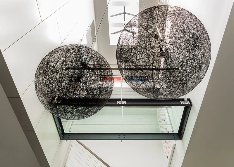 A central stairwell in a renovated townhouse in Boston featuring modern pendant lights and a glass bridge