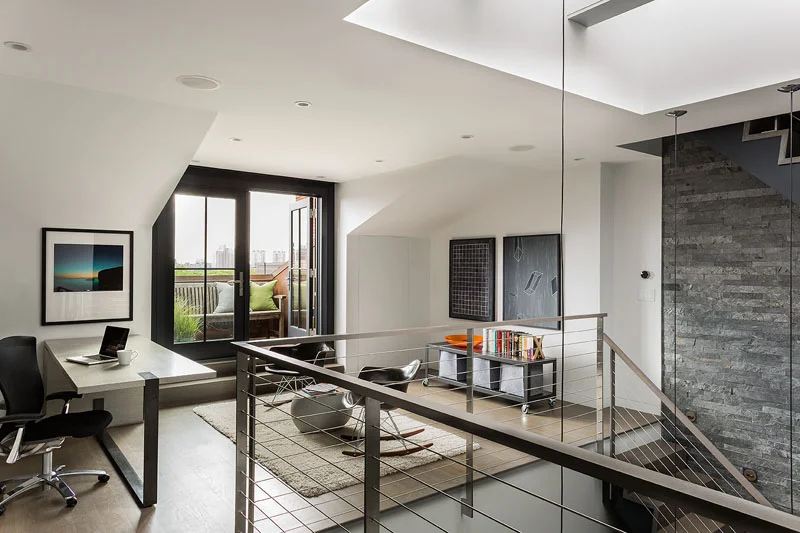 A home office in a modern townhouse renovation featuring contemporary furniture and three story rock wall below a skylight