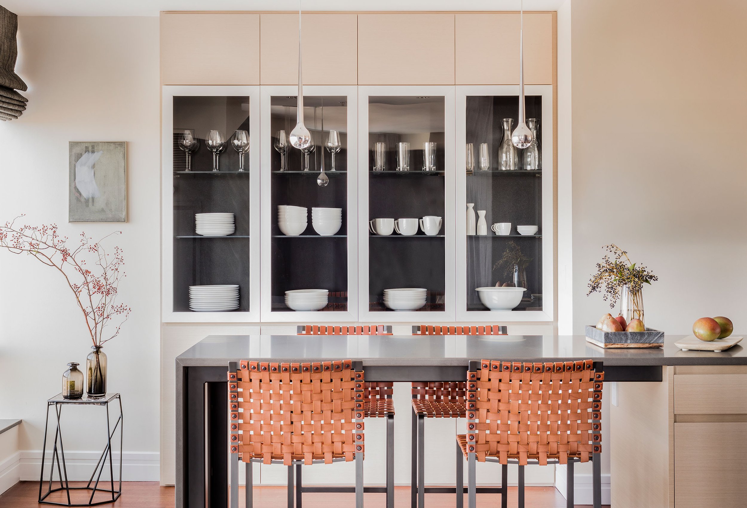A modern kitchen in a Boston Highrise featuring a dark stone and steel island and glass front cabinetry with a dark contrasting interior
