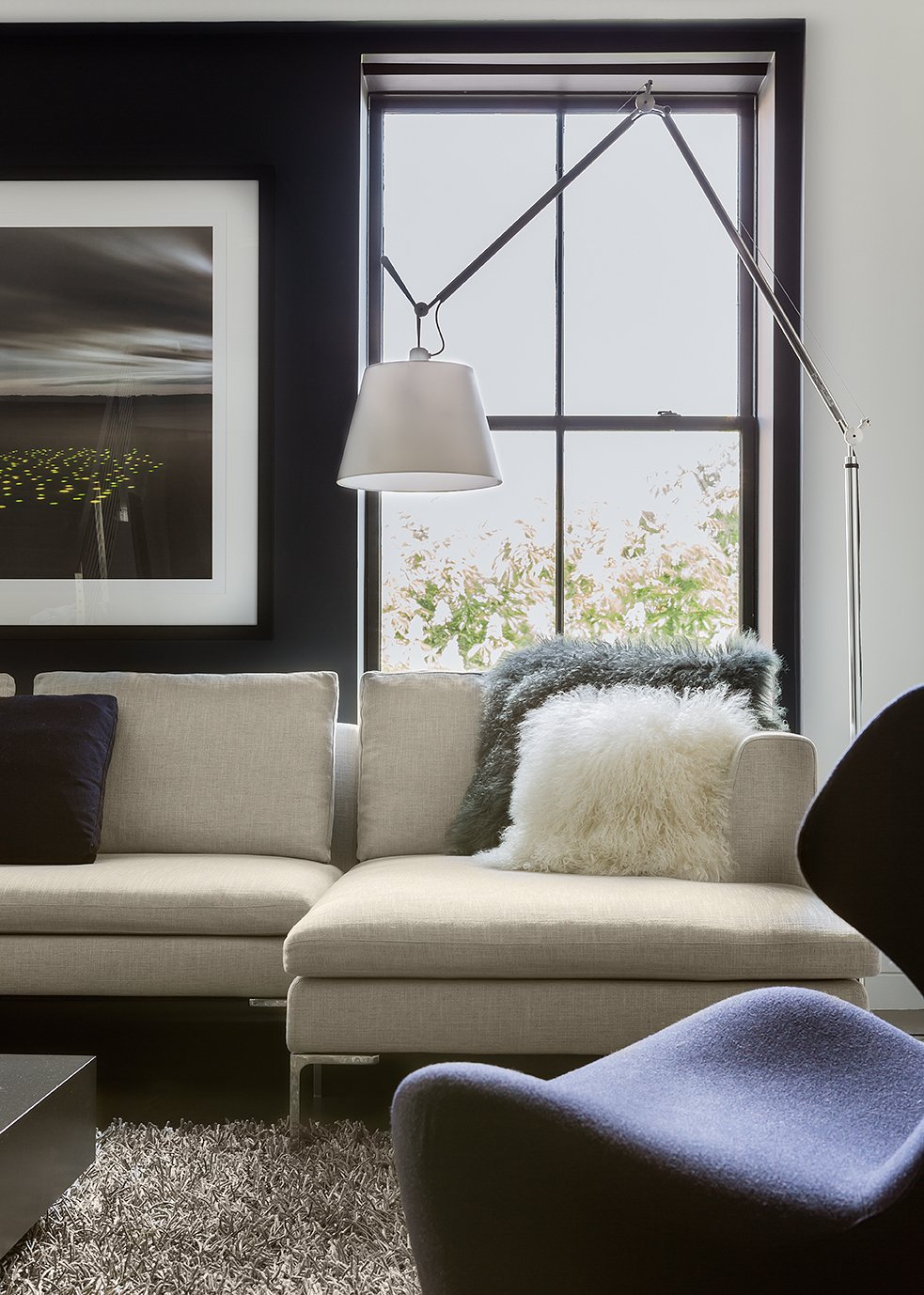 A modern sofa and  sculptural blue chair arranged near a window with contemporary black trim