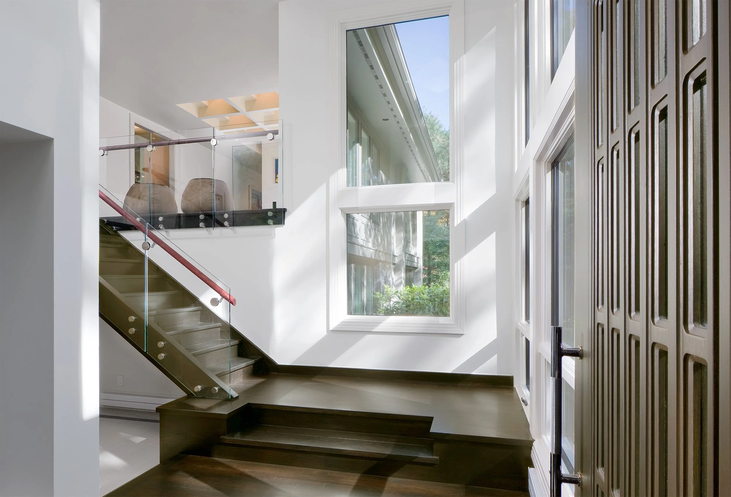An entryway in a modern house with dark floors and glass railings