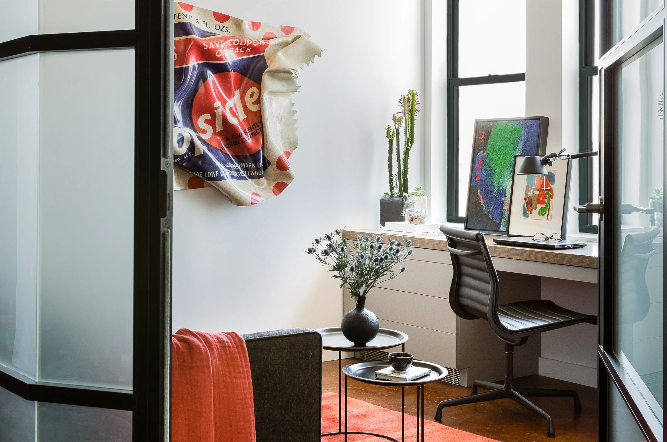 A home office with modern art and a steel and glass wall