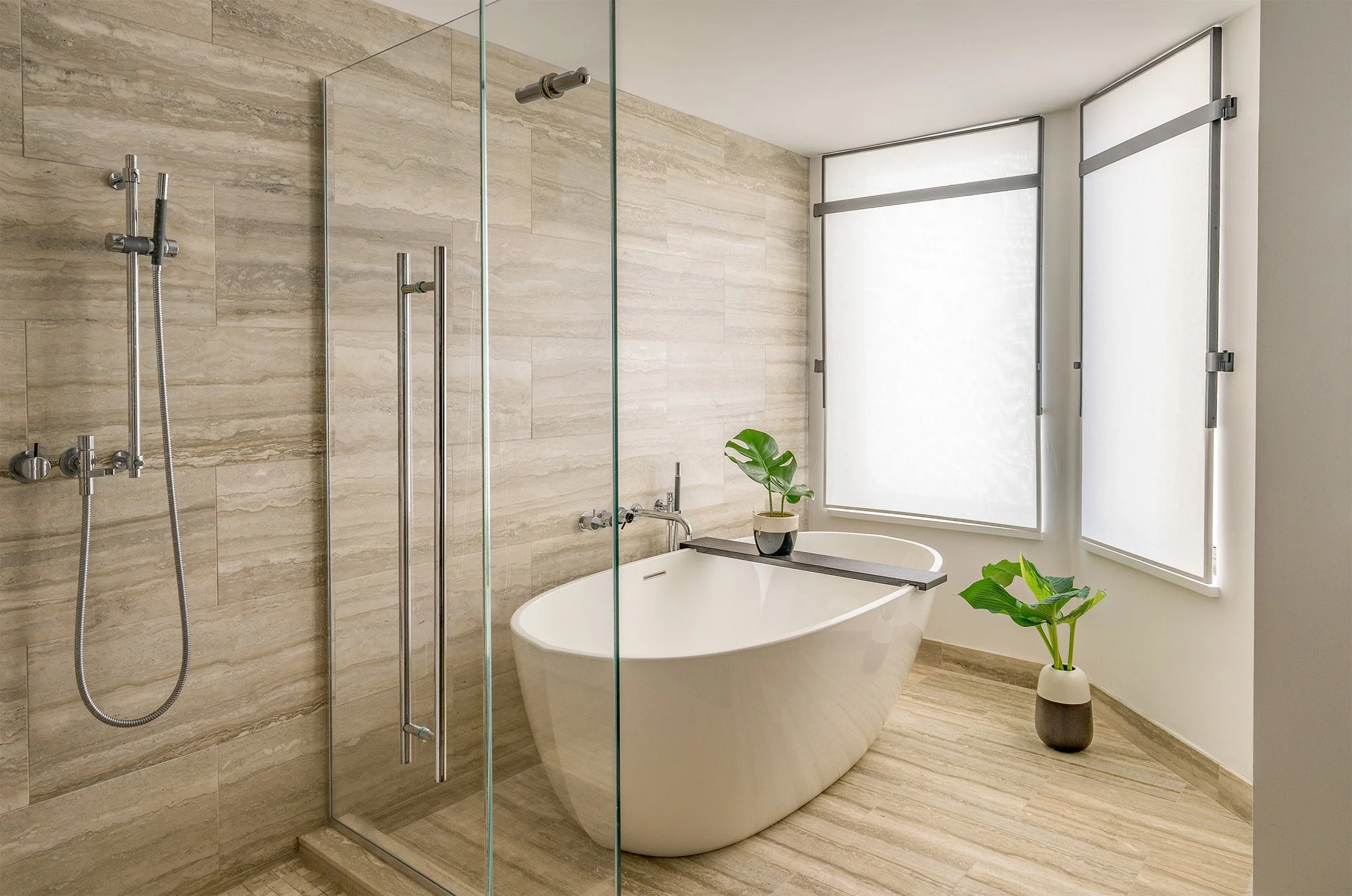 A free standing bathtub sits in a renovated primary bathroom featuring clean, modern details and warm neutral colors