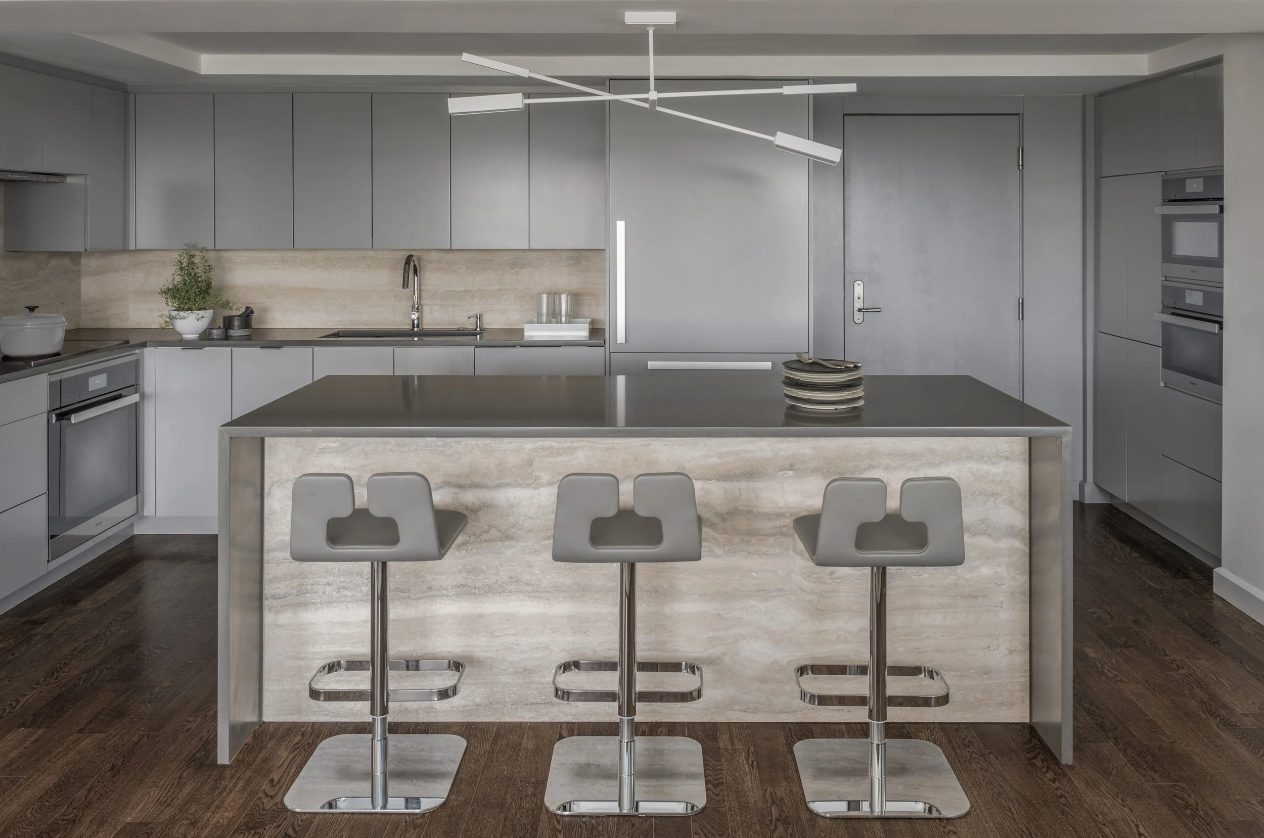 A renovated kitchen in a Boston condominium with modern gray cabinetry and a warm stone backsplash