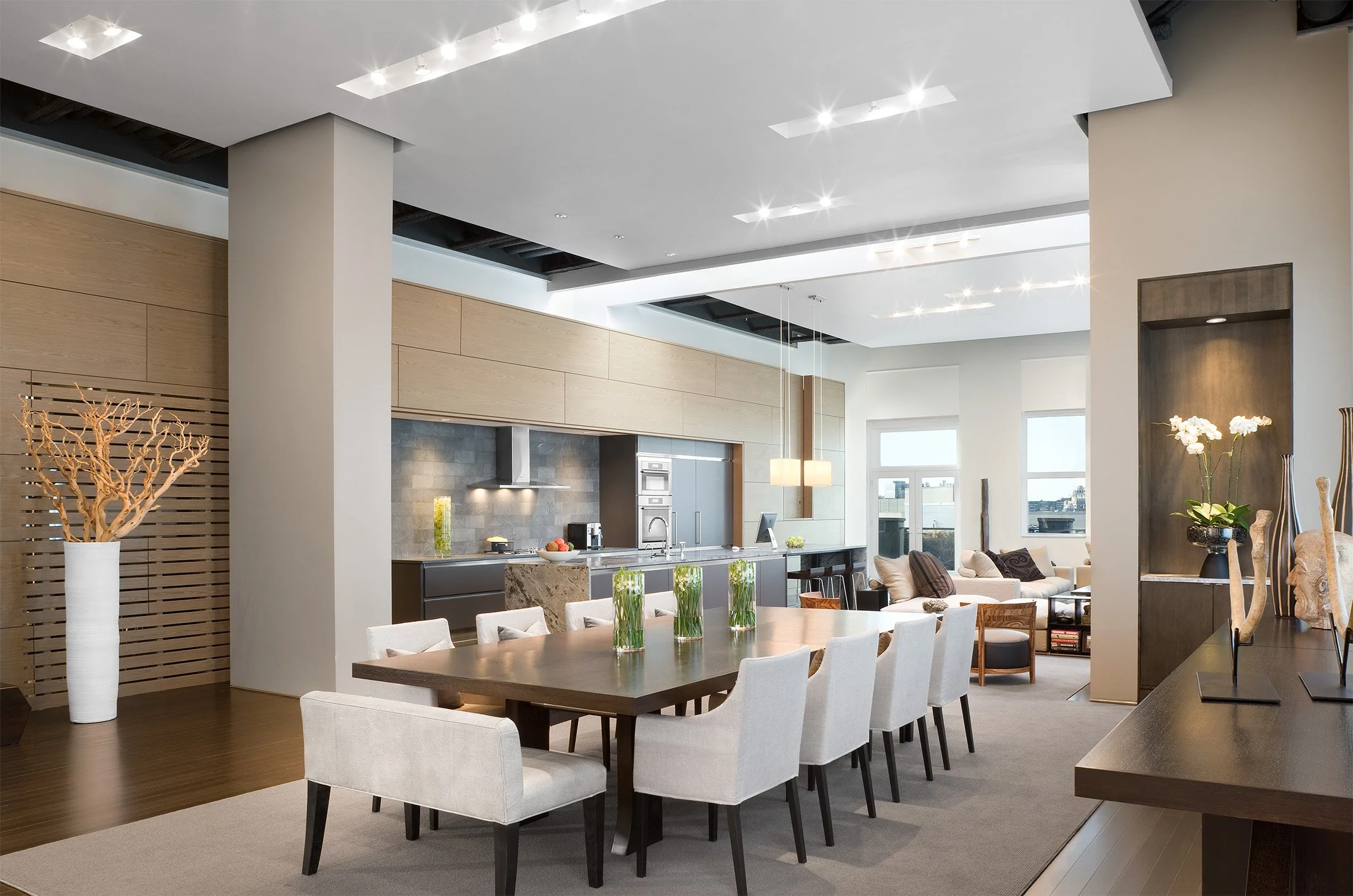 A large modern dining room table open to lofted kitchen and living room spaces beyond
