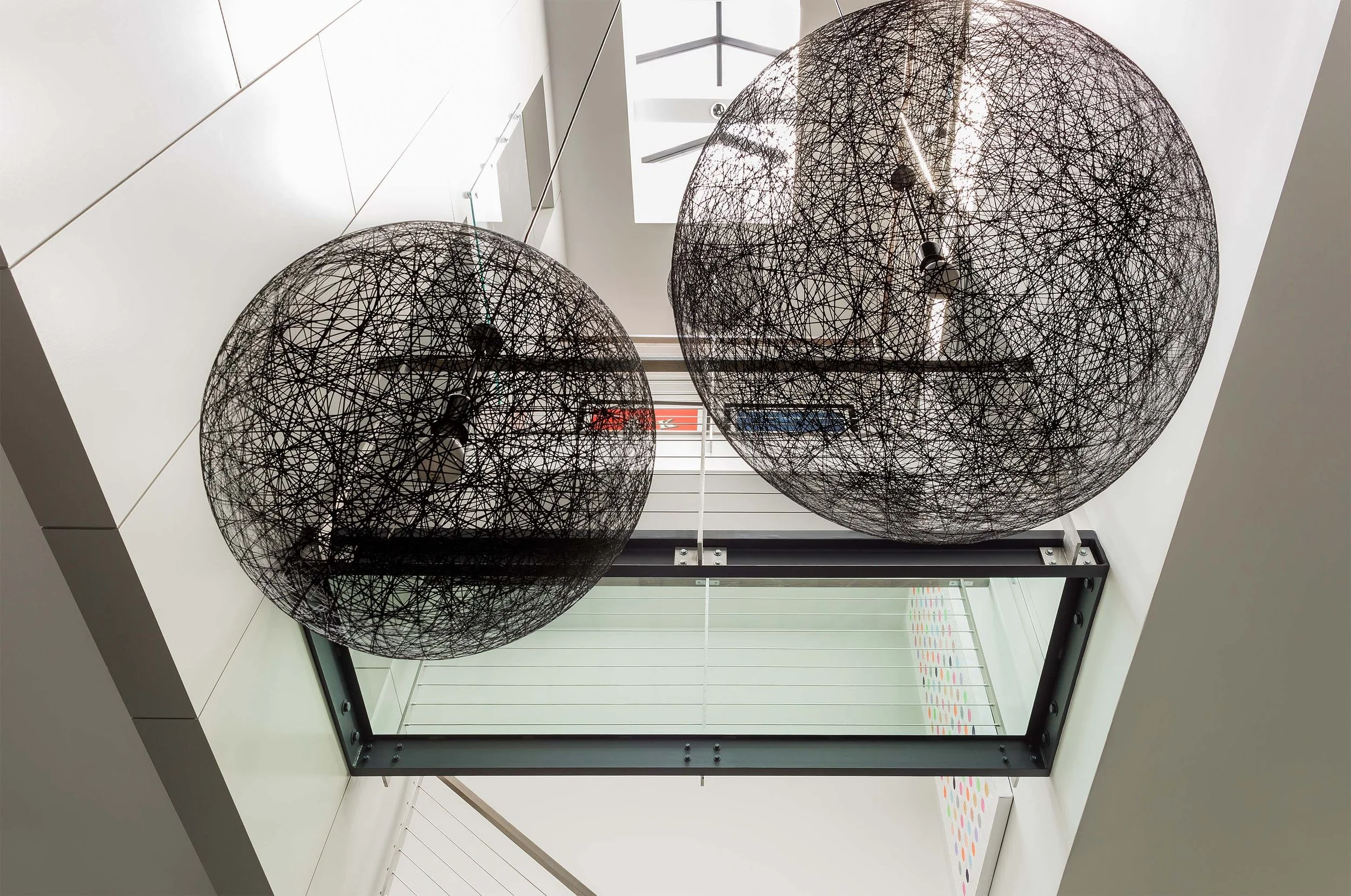 A three story stairwell acting as an atrium in a contemporary townhouse renovation, with wo large black pendent lights suspended from above