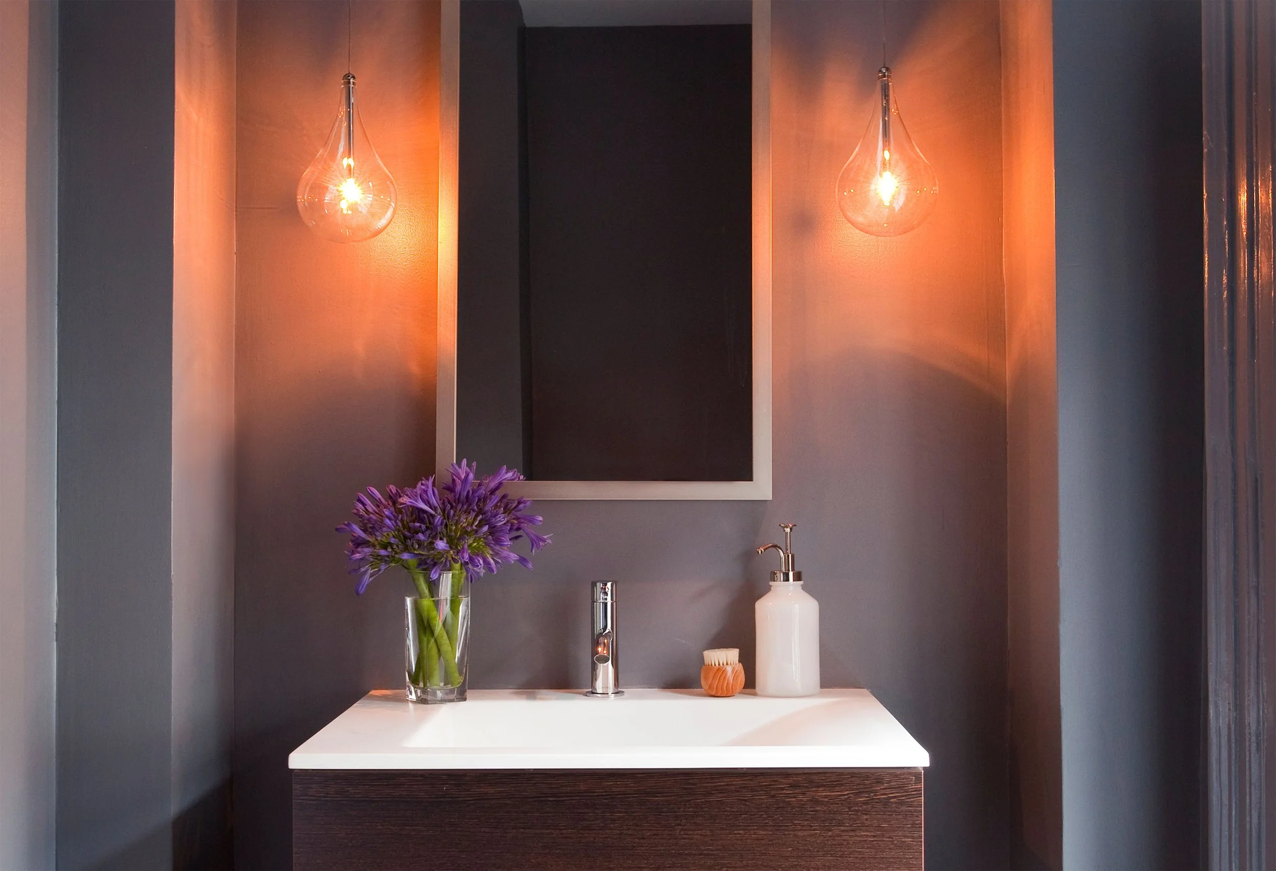 A small, moody powder room in a deep shade of gray, featuring a modern vanity and glass teardrop pendant lights