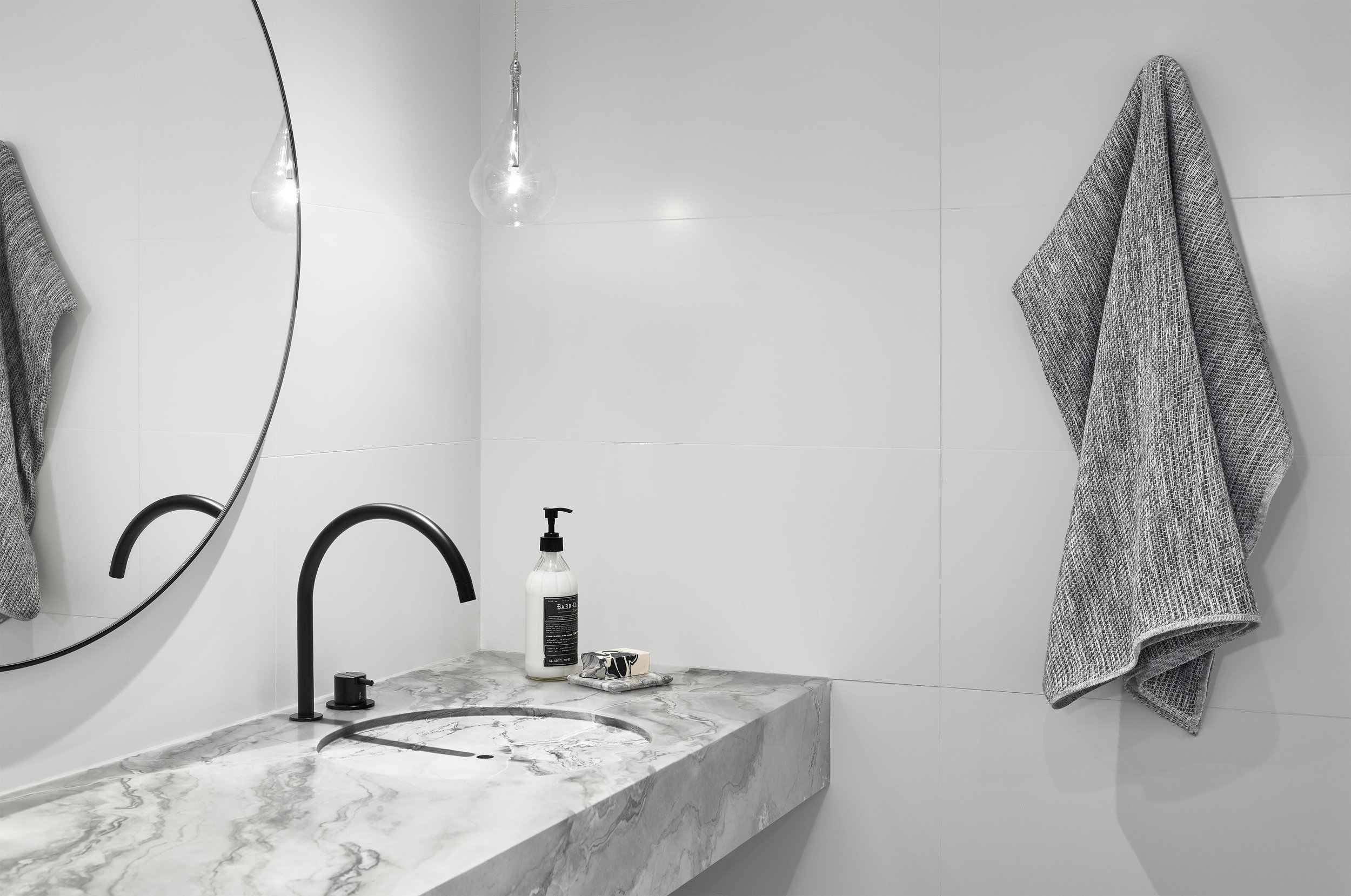 A modern bathroom featuring a custom fabricated circular quartzite sink with minimalist black faucet