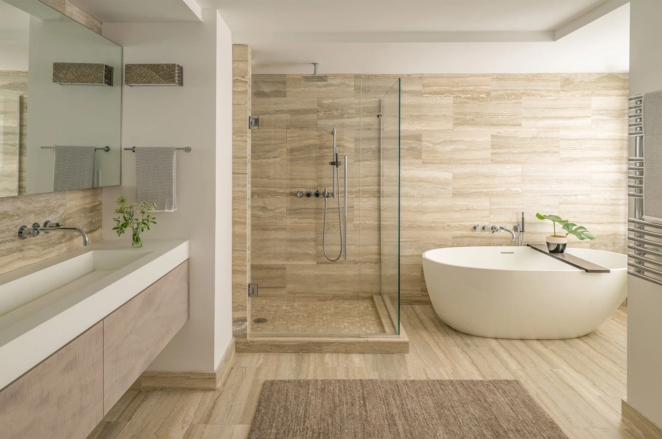 A modern primary bathroom featuring a large glass shower stall, free standing bathtub, and warm neutral colors