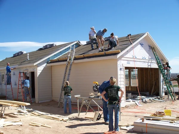 People climbing ladders and nailing shingles to the roof of a Habitat for Humanity house.